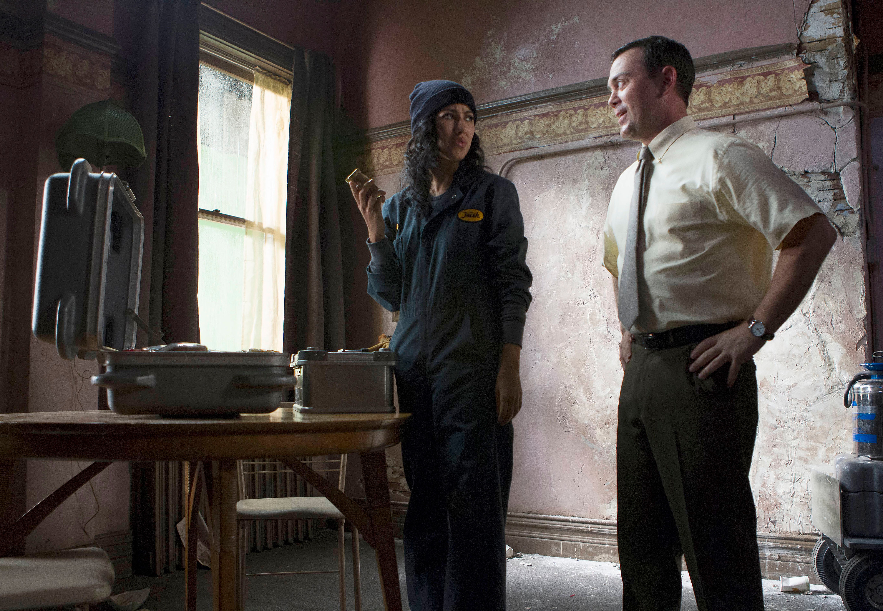 Stephanie Beatriz and Joe Lo Truglio stand near open briefcases in a decrepit room