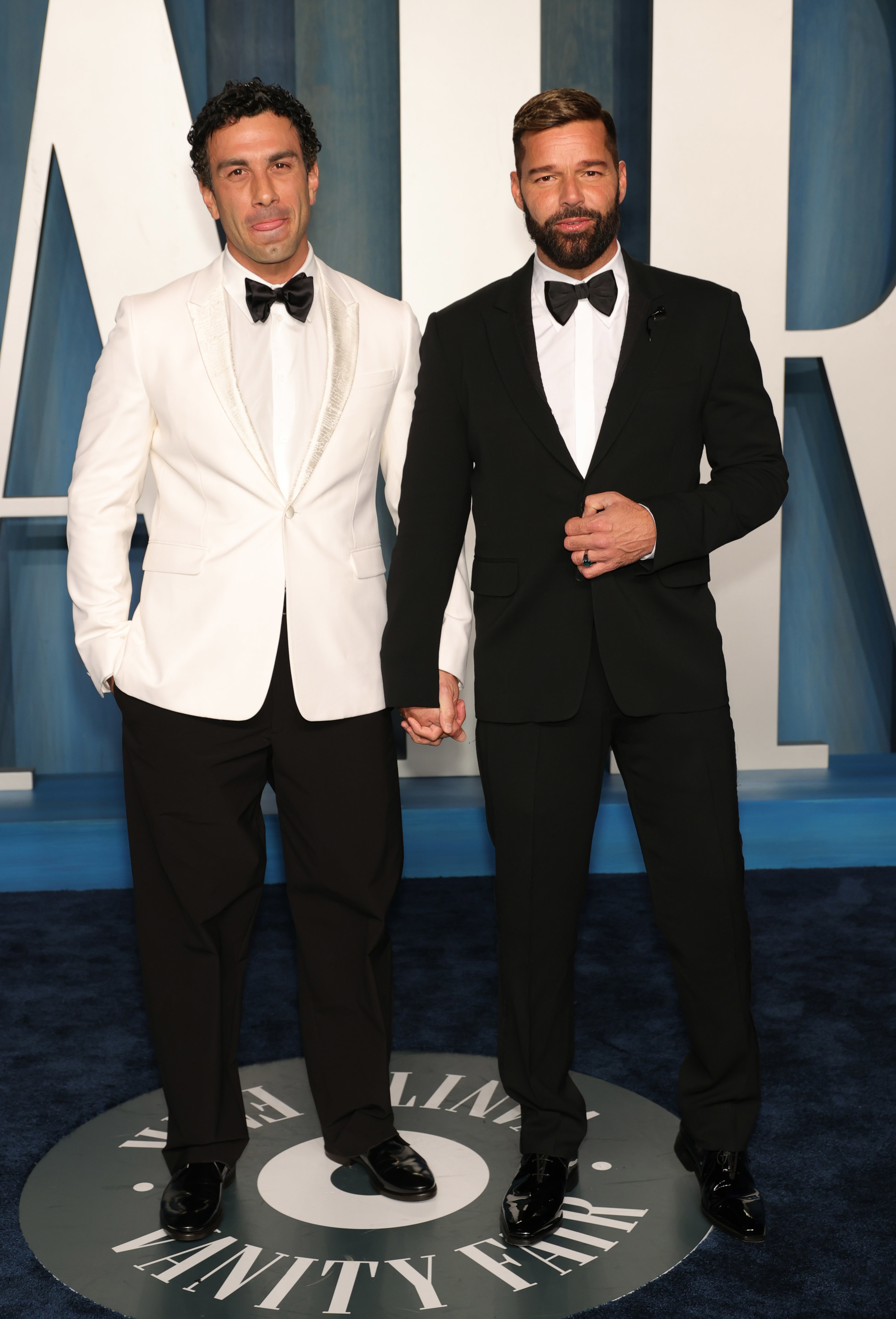 Ricky and Jwan holding hands and wearing suits and bow ties at a media event