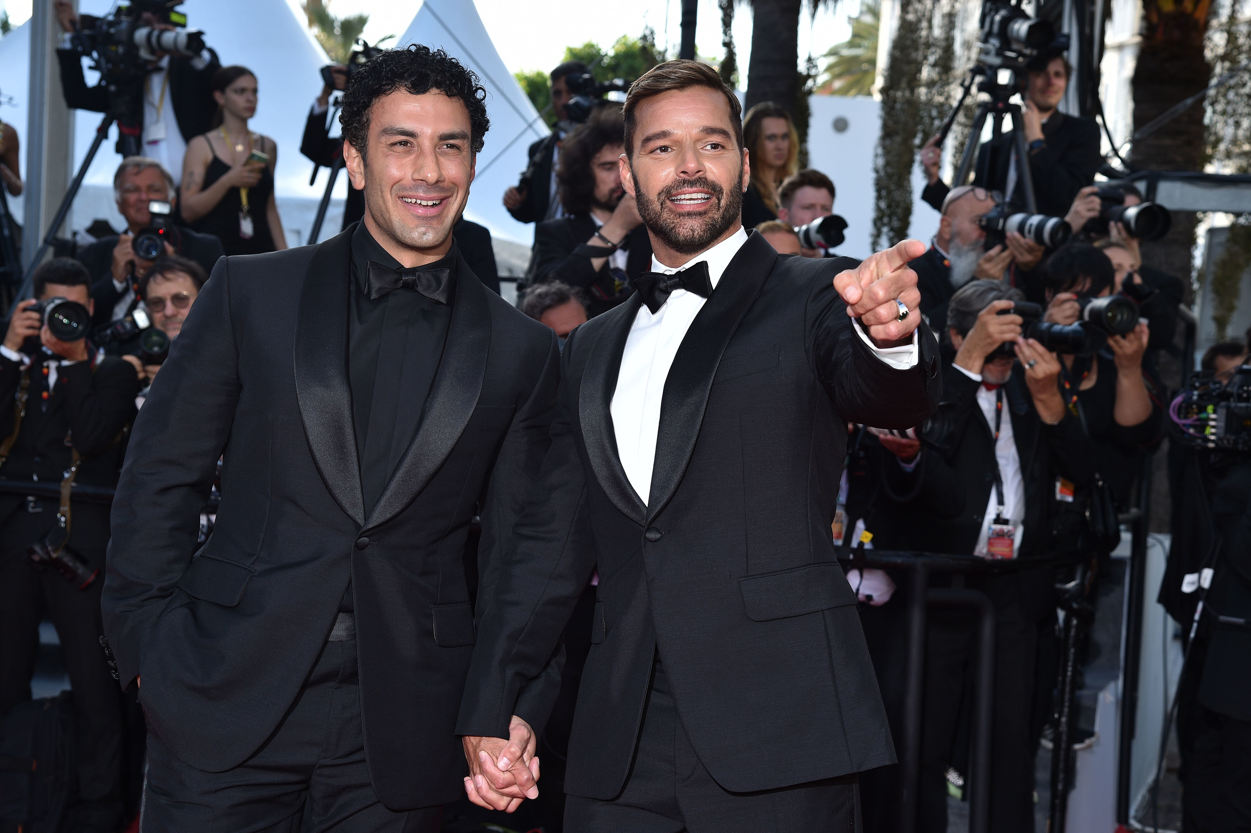 Close-up of Ricky and Jwan in tuxedos and holding hands at a media event