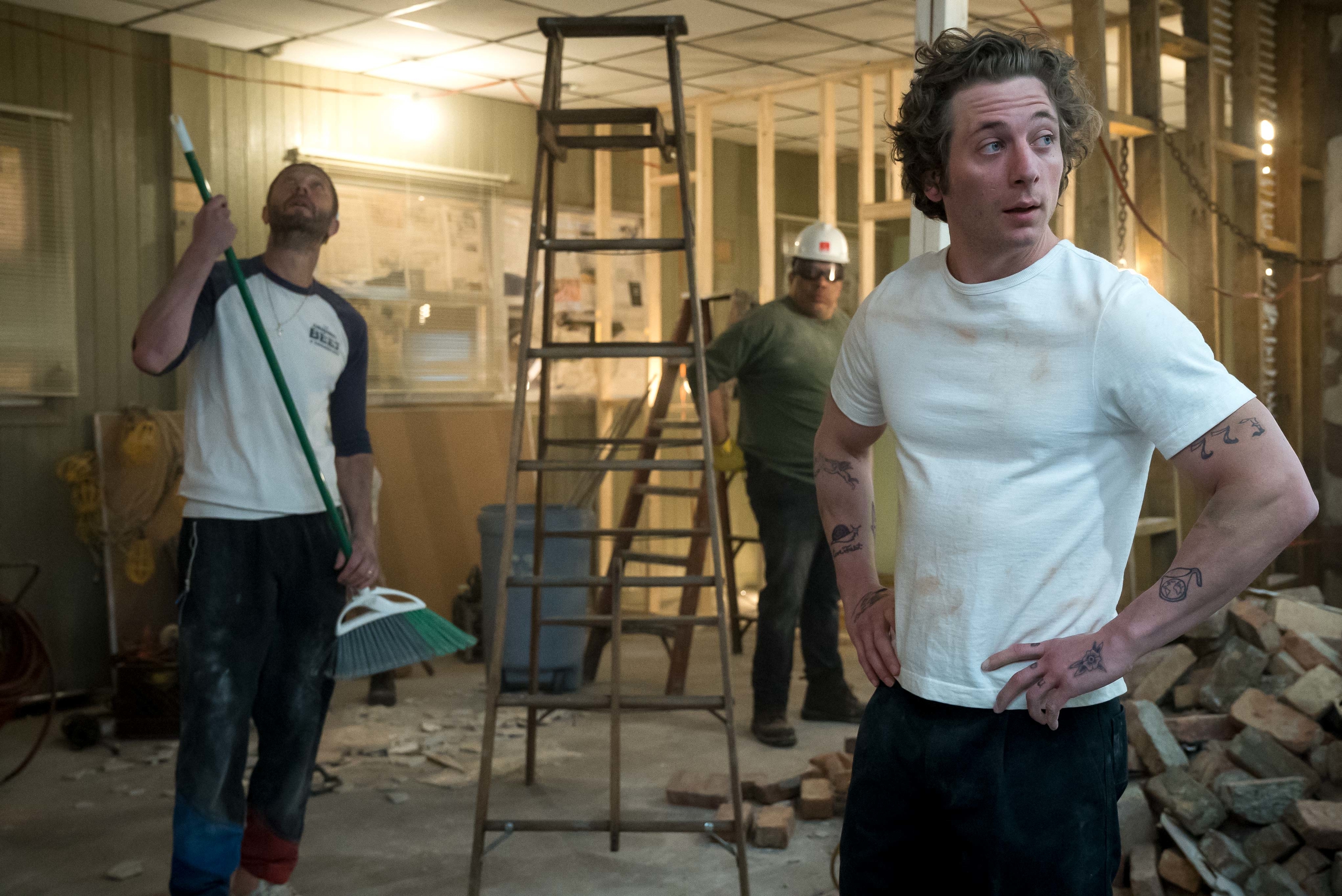 Jeremy Allen White in a construction demo scene in The Bear Season 2 with two guys in the background. Jeremy now has longer, shaggier hair