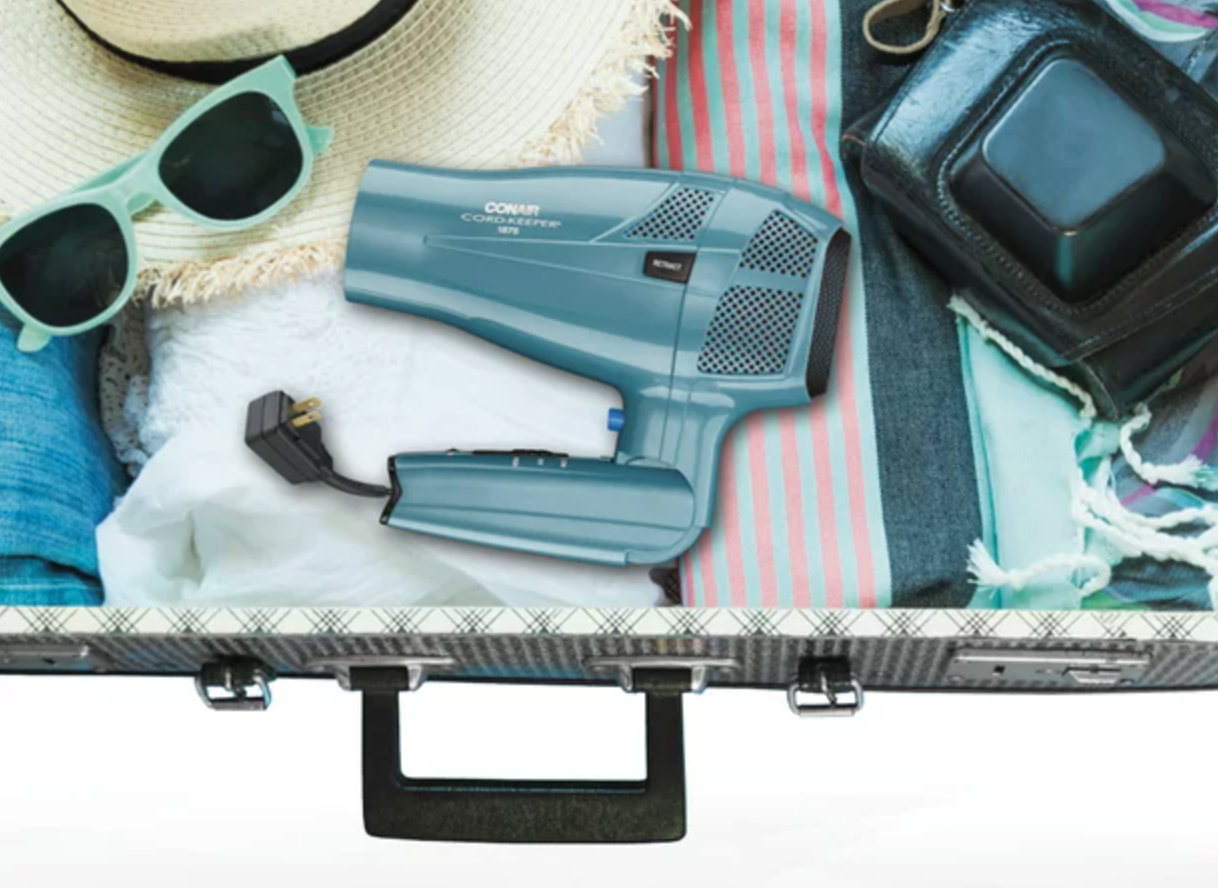 the light blue hair dryer with the handle folded in, packed in a suitcase with other travel products and clothes