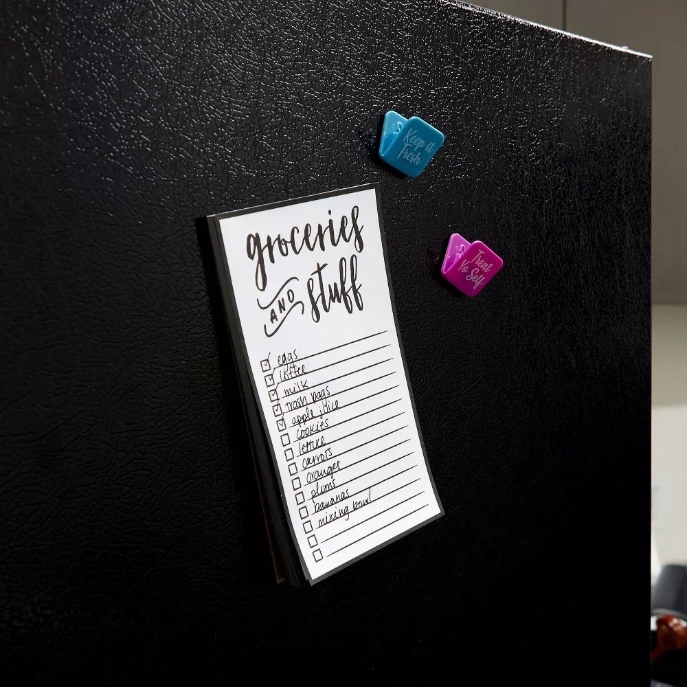 The magnetic grocery list shown on a black fridge.