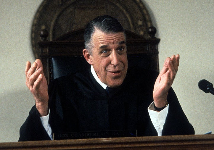 Gwynne as Judge Chamberlain, holding his hands up and talking in court