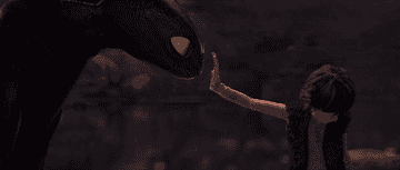 Hiccup from How to Train Your Dragon extends his hand to touch the nose of Toothless, the Night Fury dragon