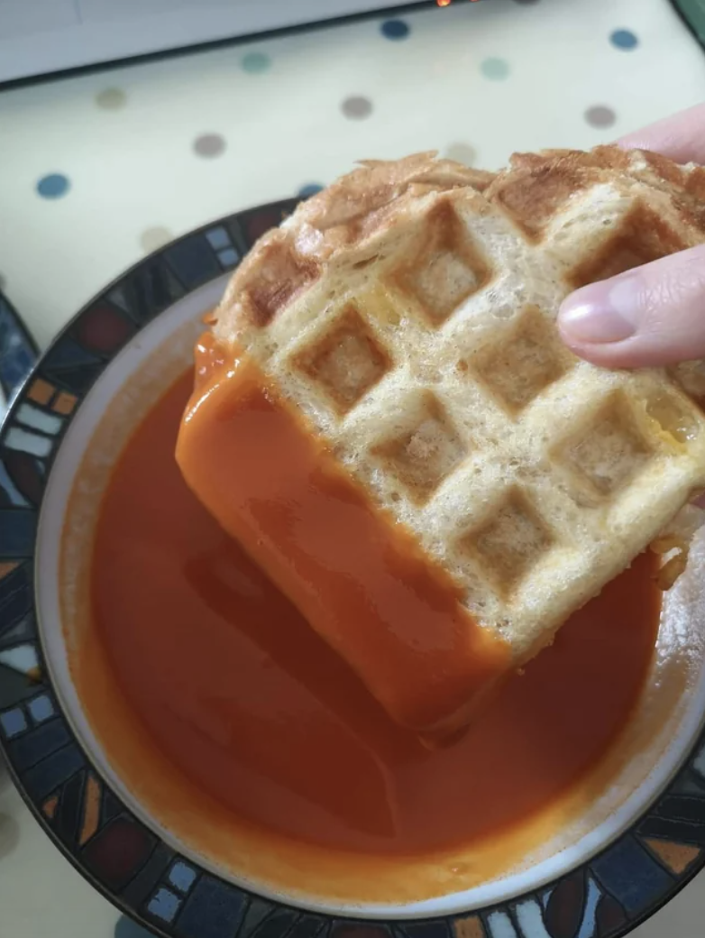 Close-up of a waffle grilled cheese being dipped into tomato soup