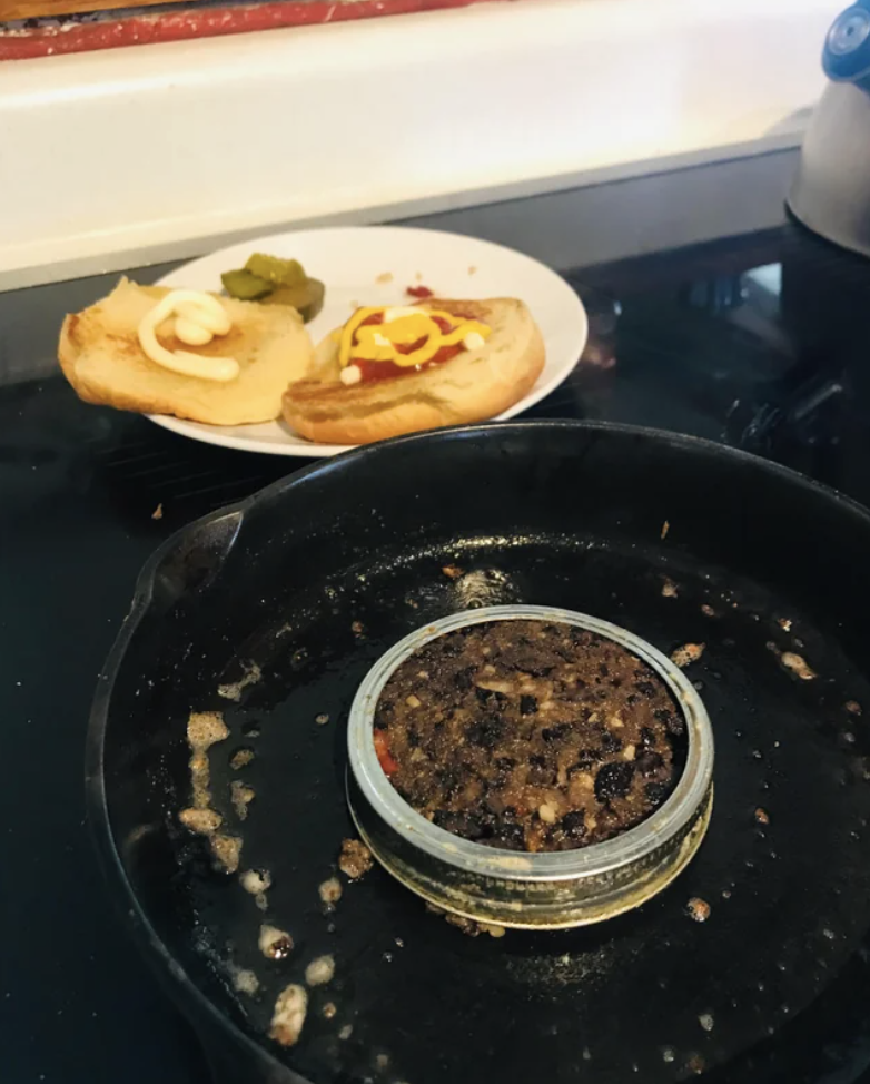 A Mason jar lid over a burger cooking in a pan