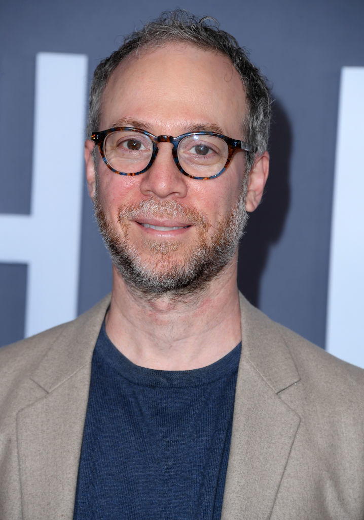 wearing glasses and a blazer with greying hair and beard