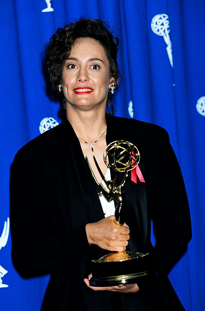 curly hair pinned back and wearing a blazer while holding an award