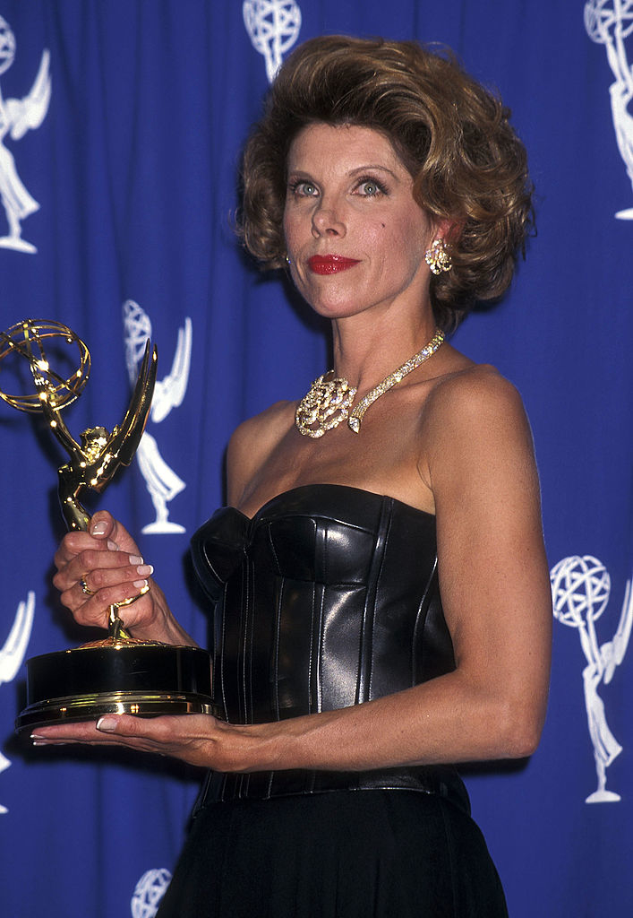 with short curled hair and a strapless dress holding an award