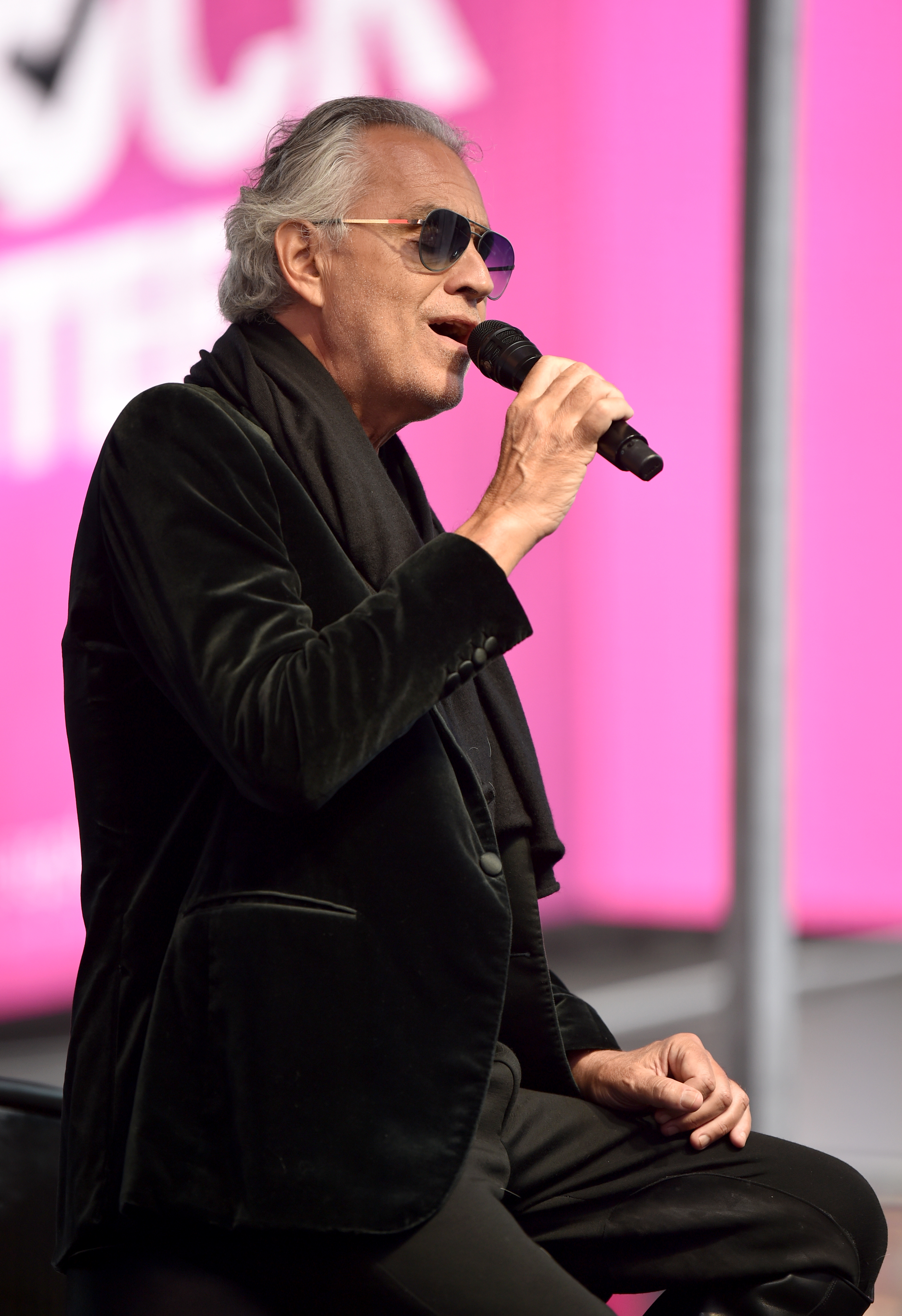 Close-up of Andrea seated and singing into a microphone he&#x27;s holding