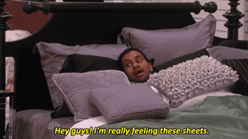 Tom from Parks and Recreation in a bed saying &quot;Hey guys! I&#x27;m really feeling these sheets.&quot;