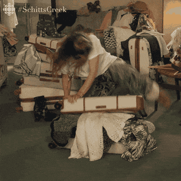 gif of Alexis Rose on Schitt&#x27;s Creek sitting on a suitcase trying to force it shut