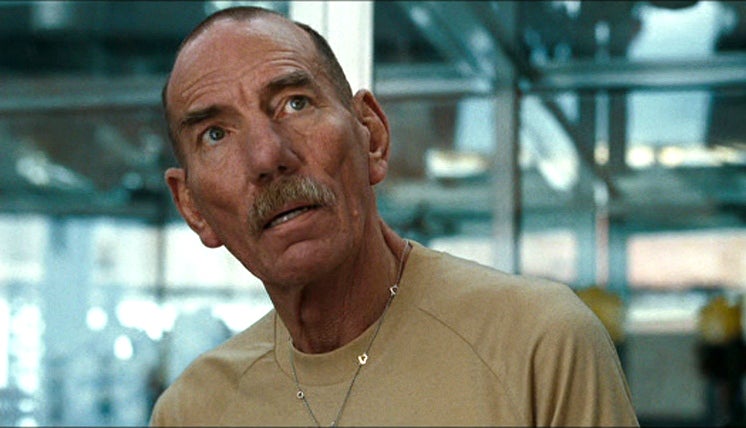 Postlethwaite with a shaved head and mustache in the town