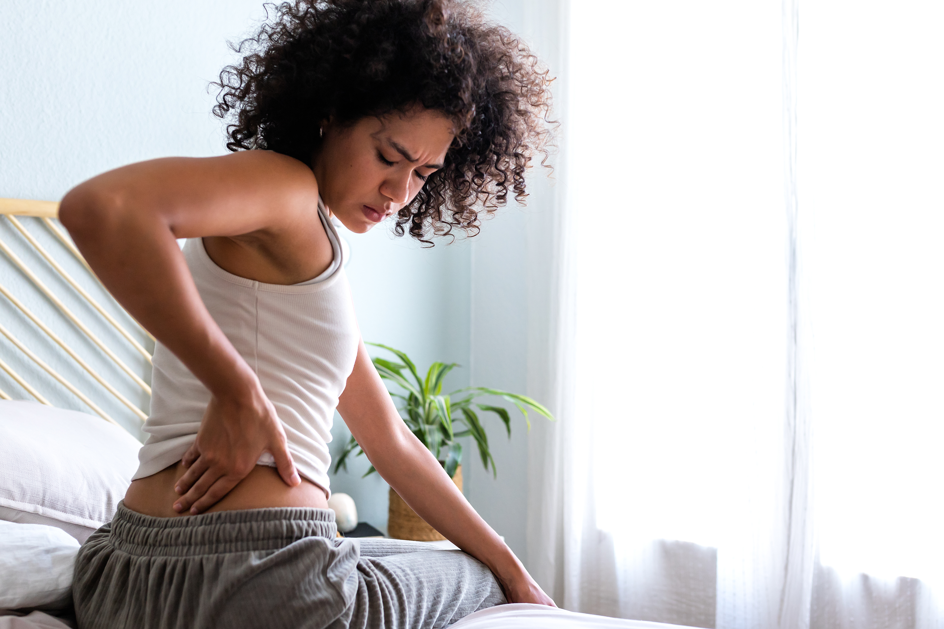 A woman sitting on a bed and touching her back in pain