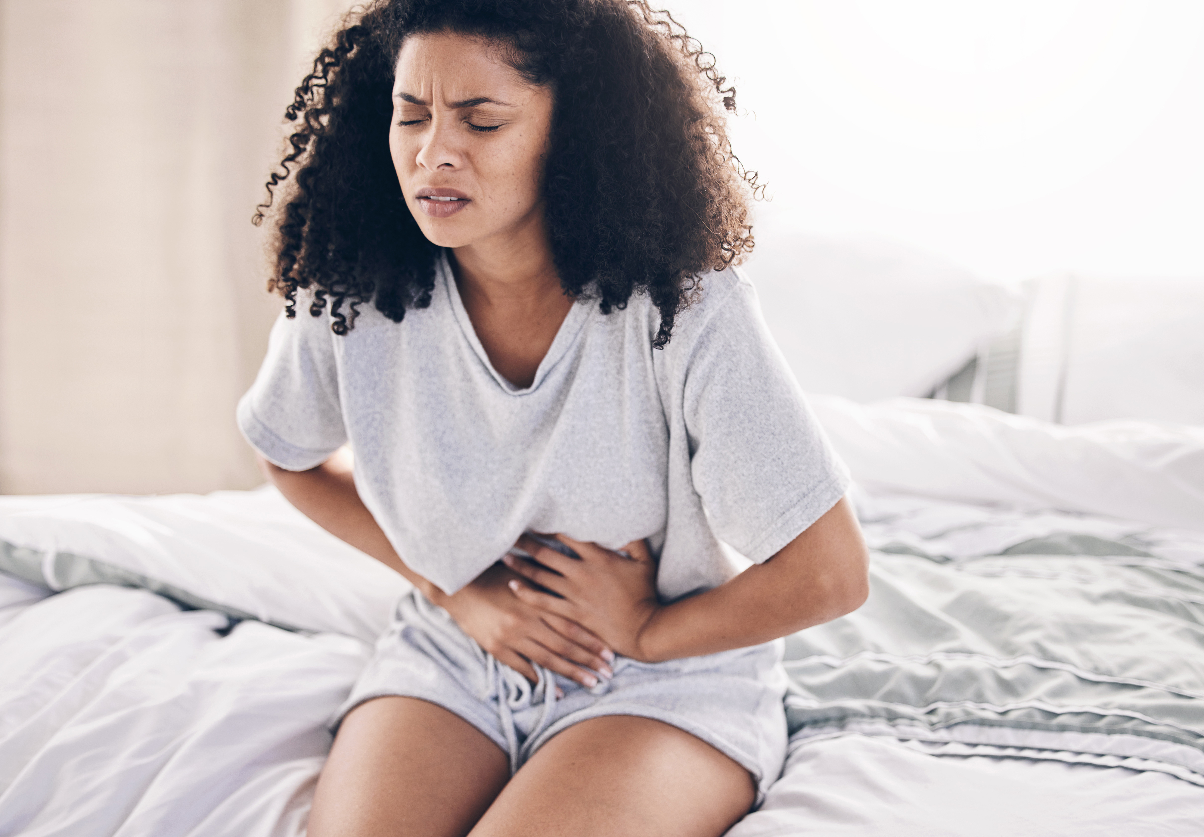 A woman sitting on a bed and clutching her stomach in pain