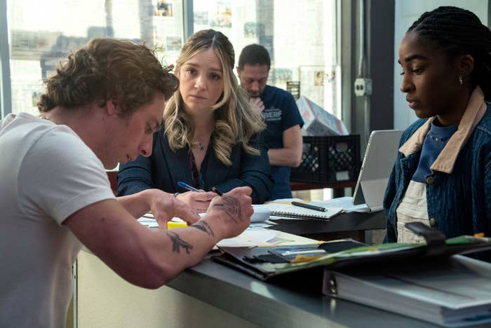 Jeremy Allen White writing on a countertop with Abby Elliott and Ayo Edebiri standing near him in The Bear