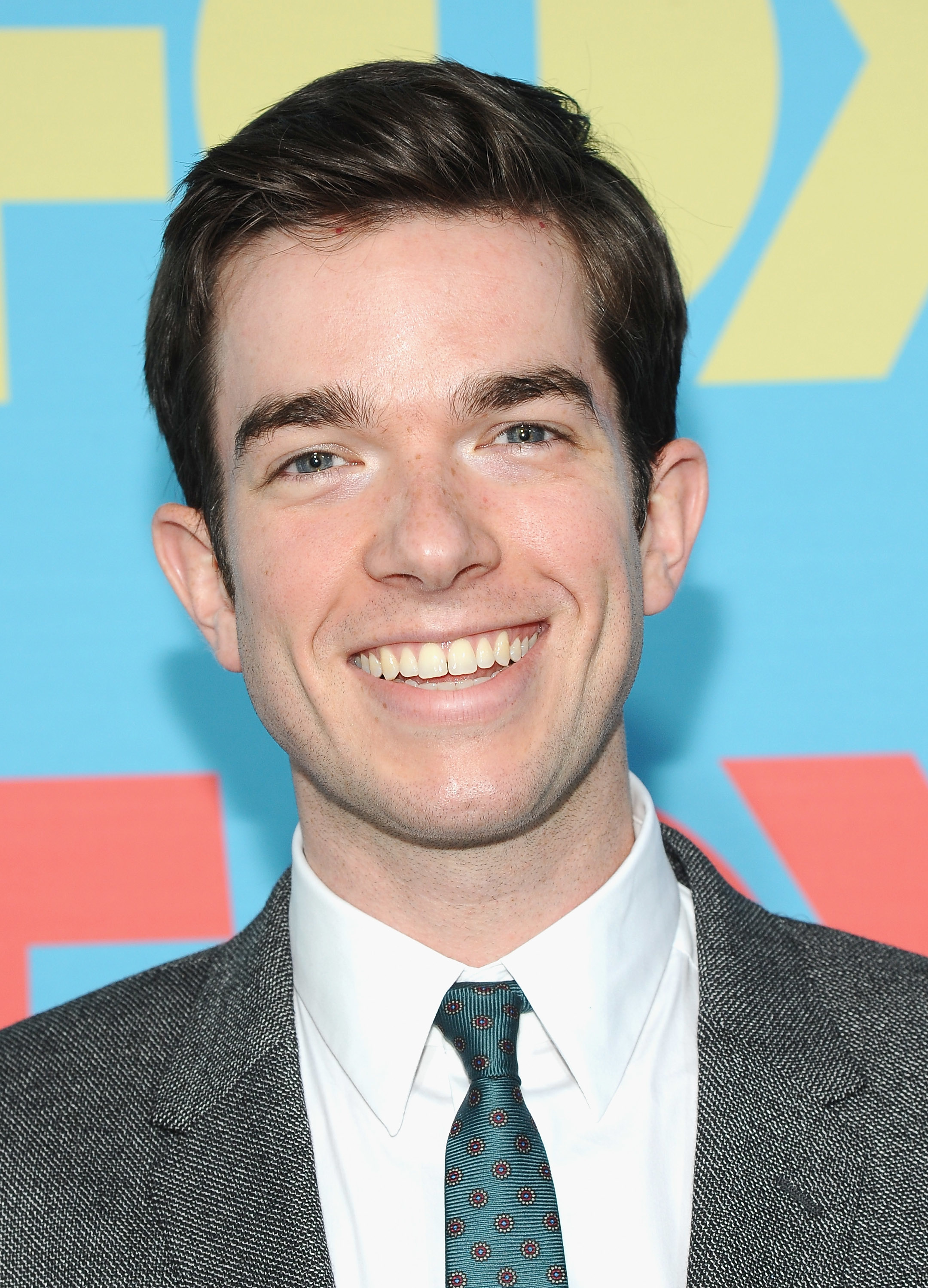 John Mulaney at the FOX Fanfront in 2014 in a gray suit, white collared shirt, and dotted tie