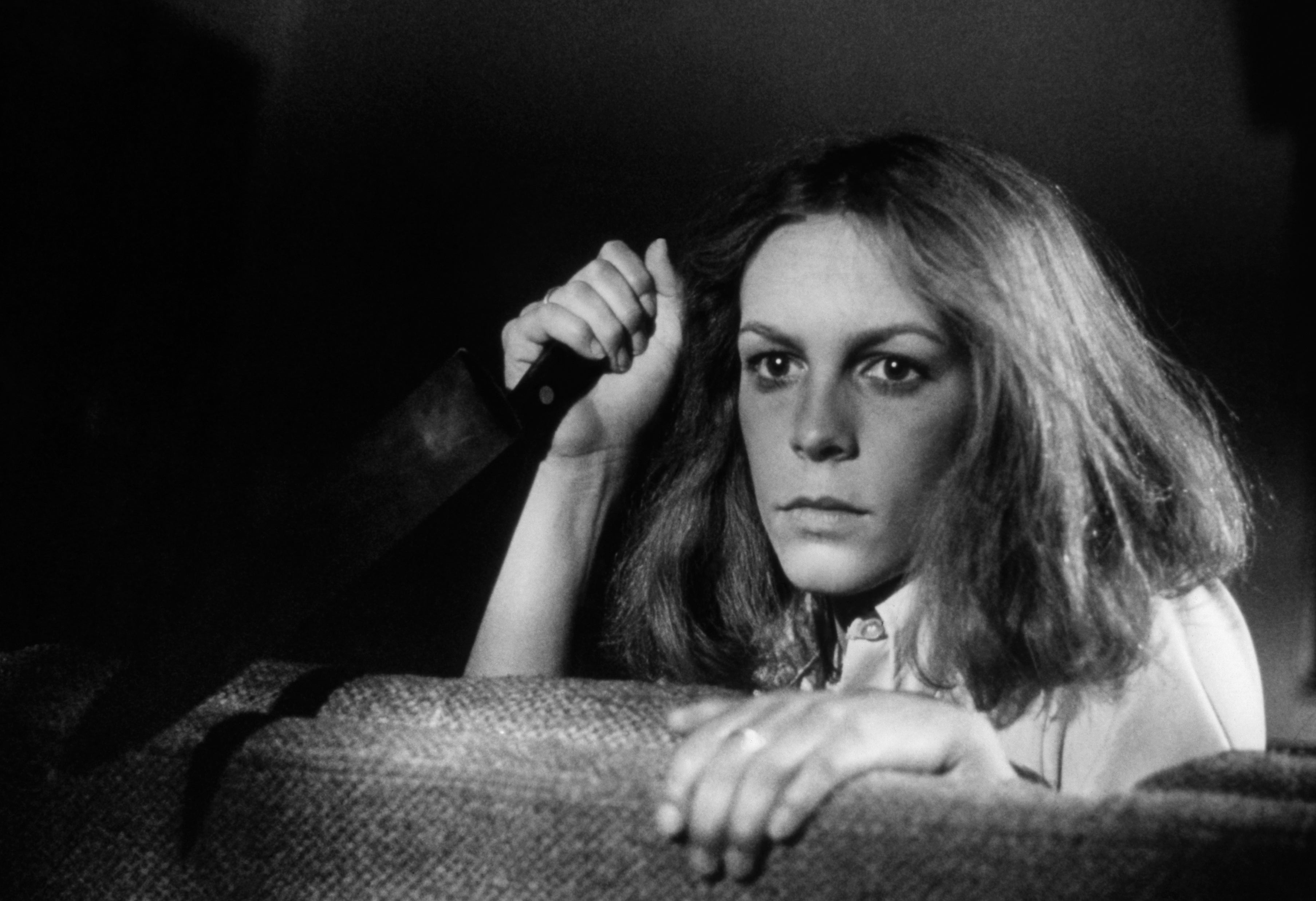 Jamie Lee Curtis holding a knife as she looks over the back of a couch in Halloween