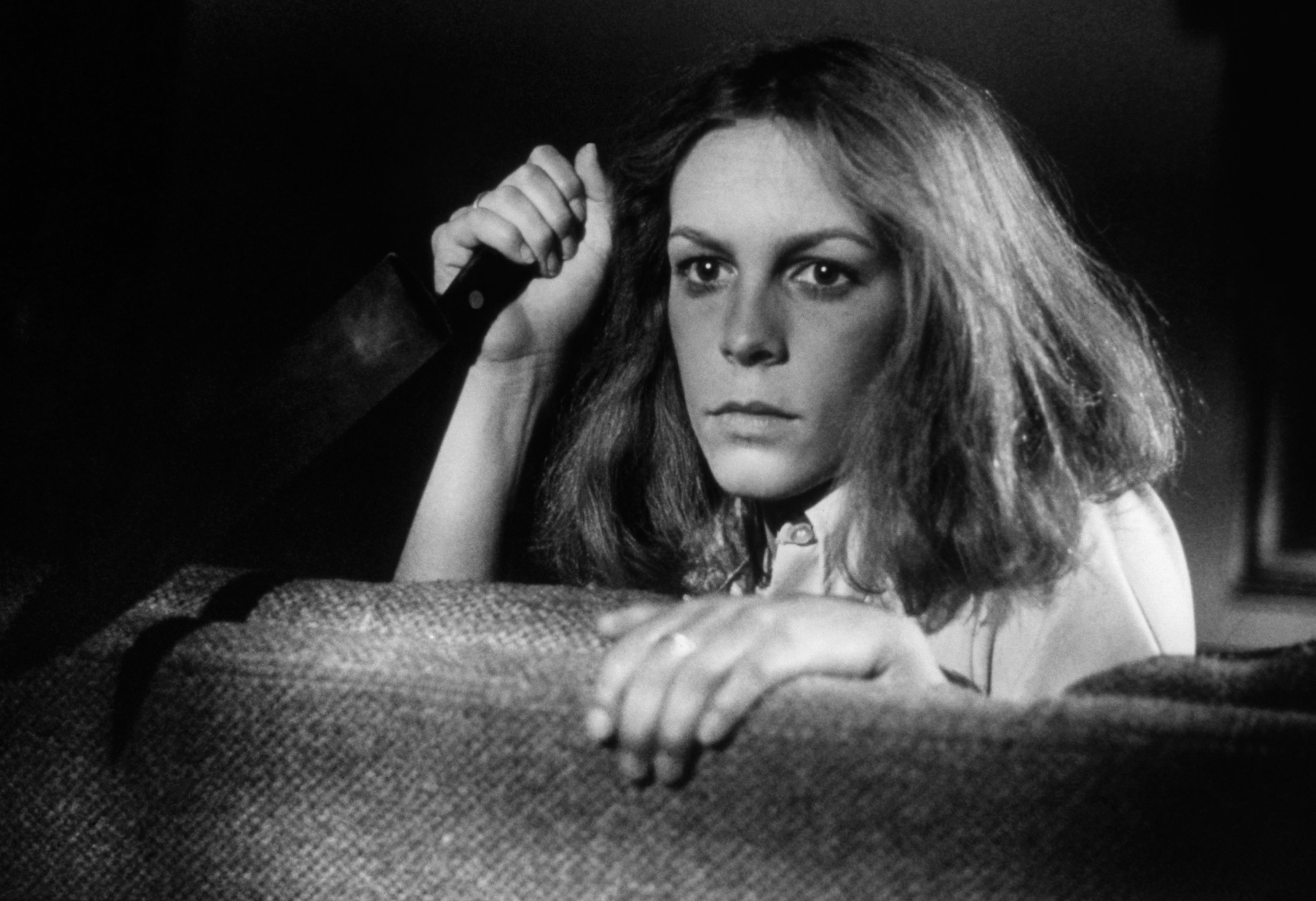 Jamie Lee Curtis holding a knife as she looks over the back of a couch in Halloween