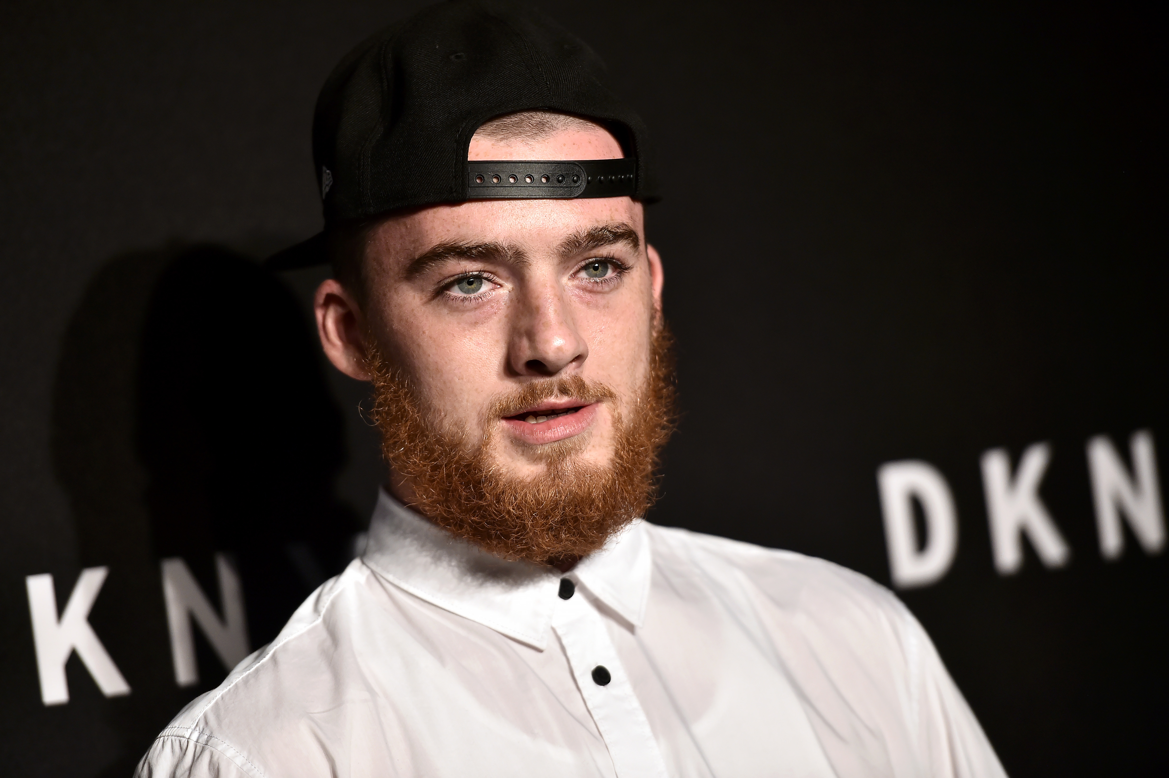 Close-up of Angus at a press event wearing a backward cap