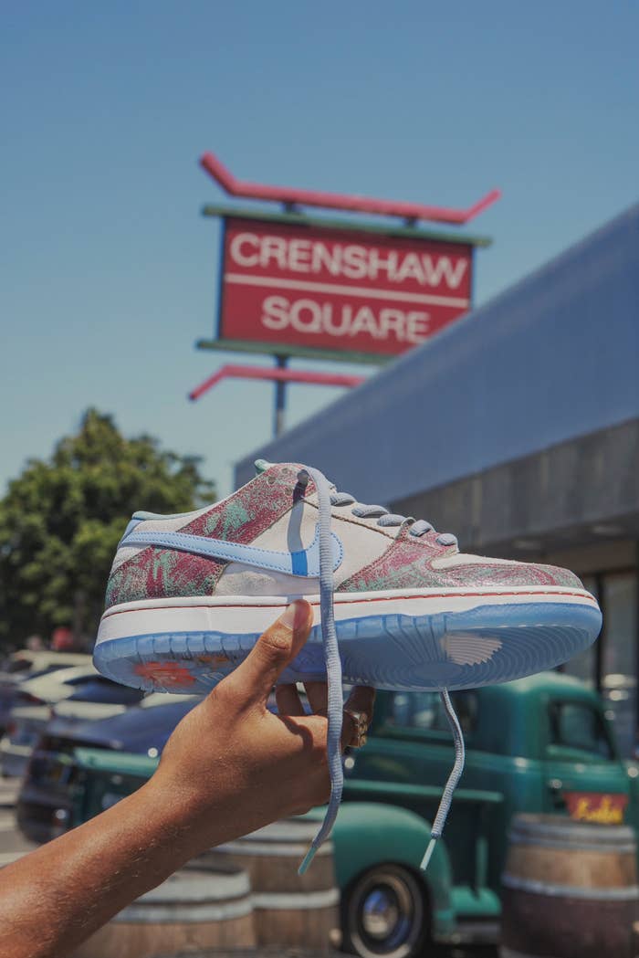 The Crenshaw Skate Club x Nike SB Dunk Low in front of the Crenshaw Square sign it&#x27;s inspired by.