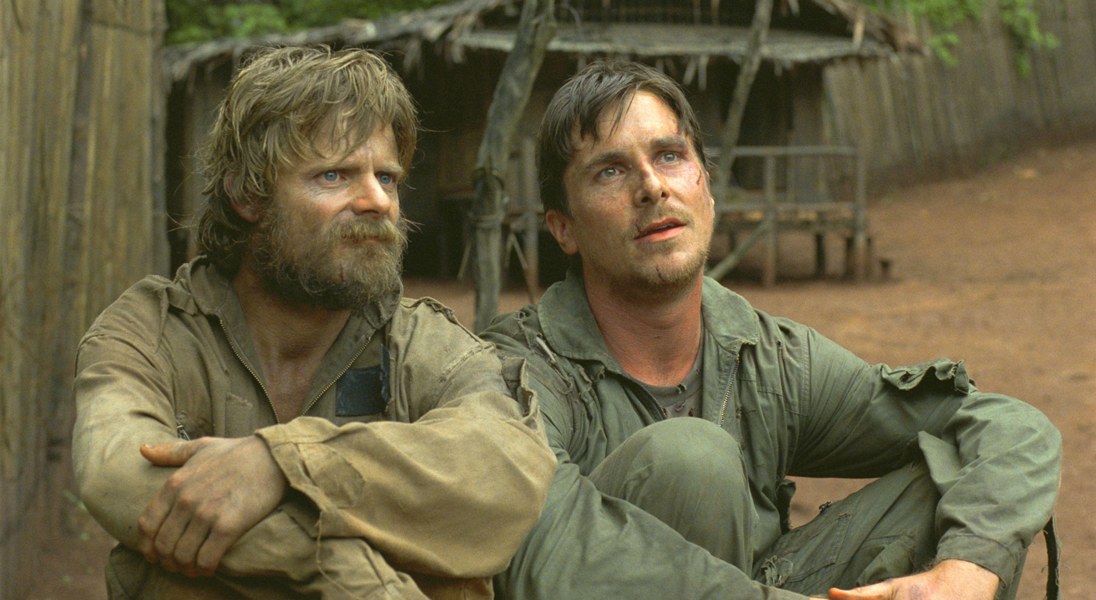 Christian Bale and Steve Zahn sit in a prisoner-of-war camp in dirty ragged clothes