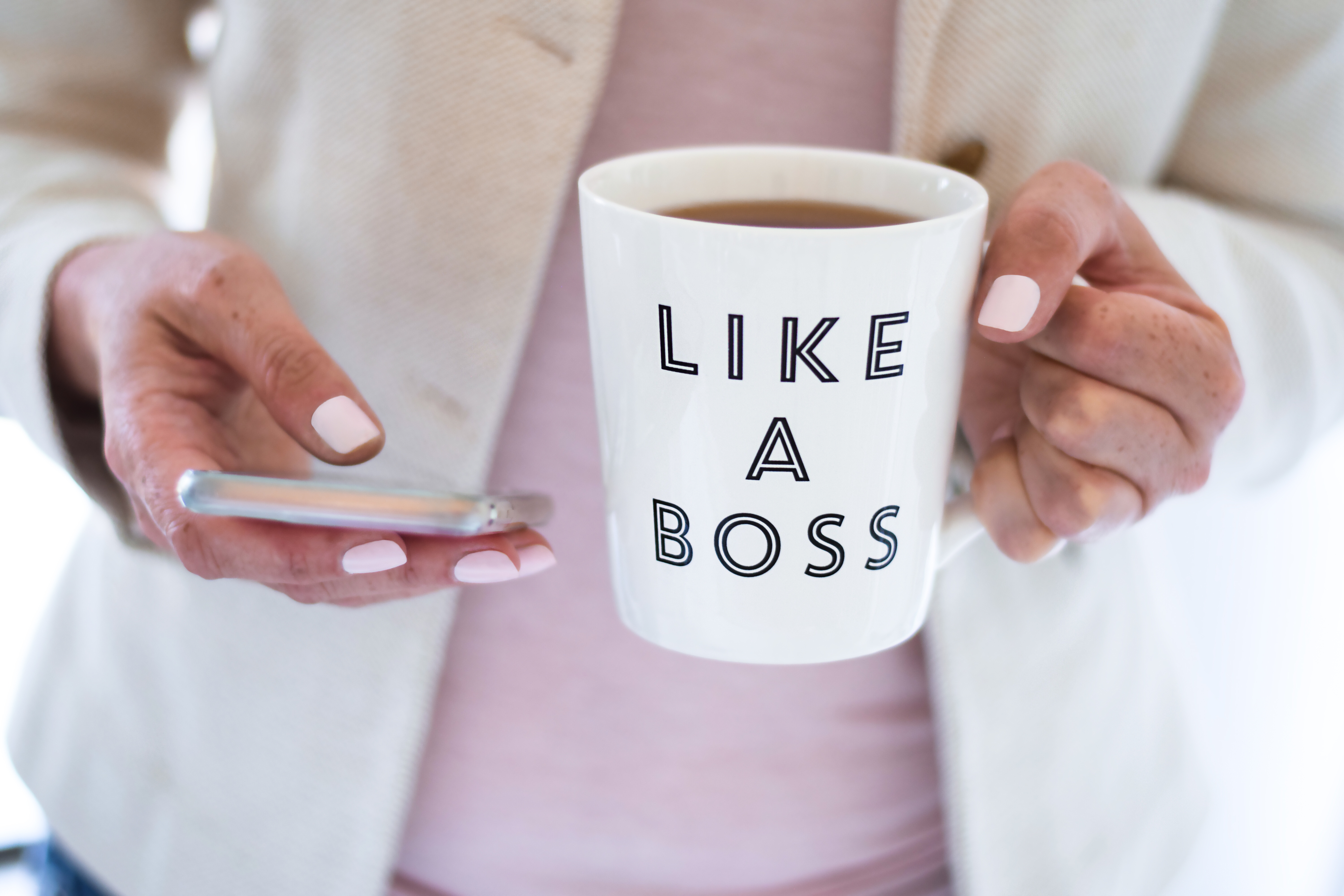 woman wearing pink business attire holding a mug that says like a boss