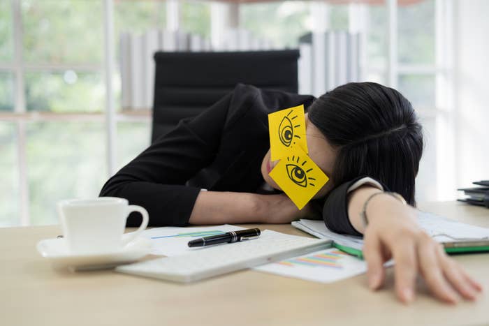 woman sleeping on her desk with post it notes stuck over her eyes