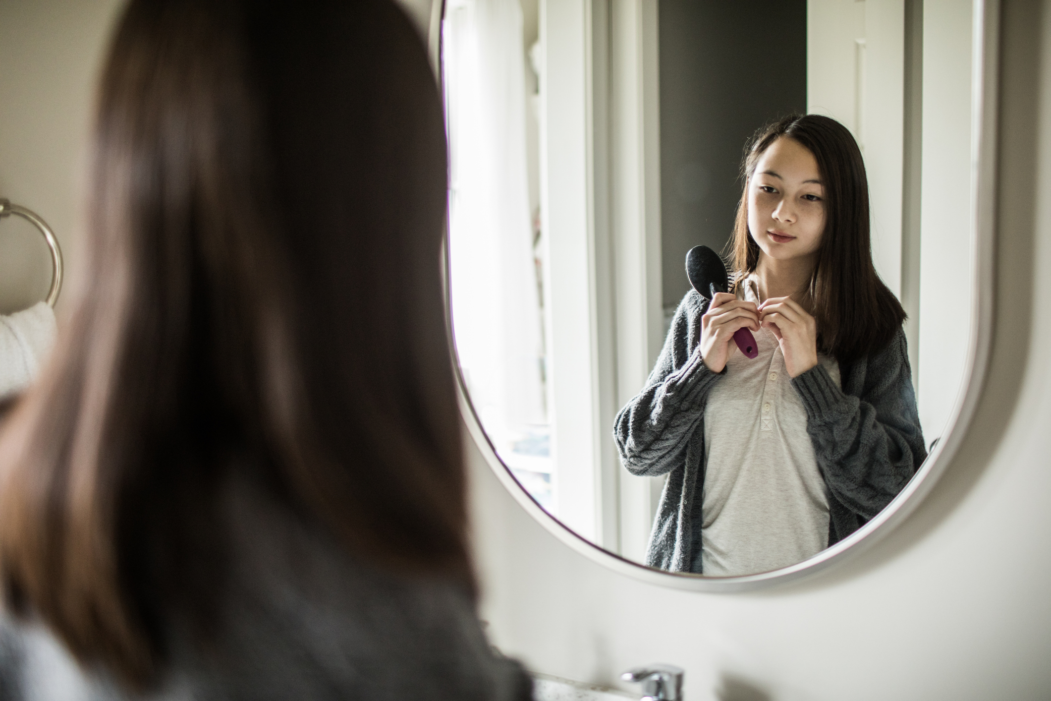 A teenage girl is looking at herself in a mirror