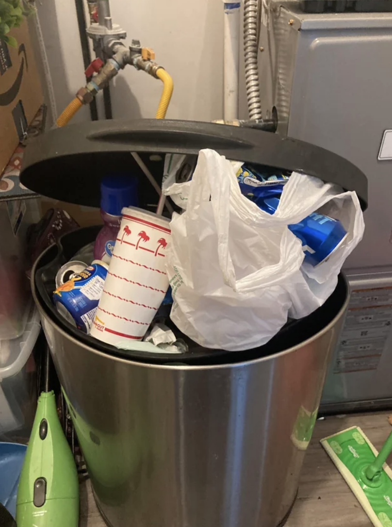 The trash can is so full that the lid can&#x27;t close and pieces of trash are close to spilling out