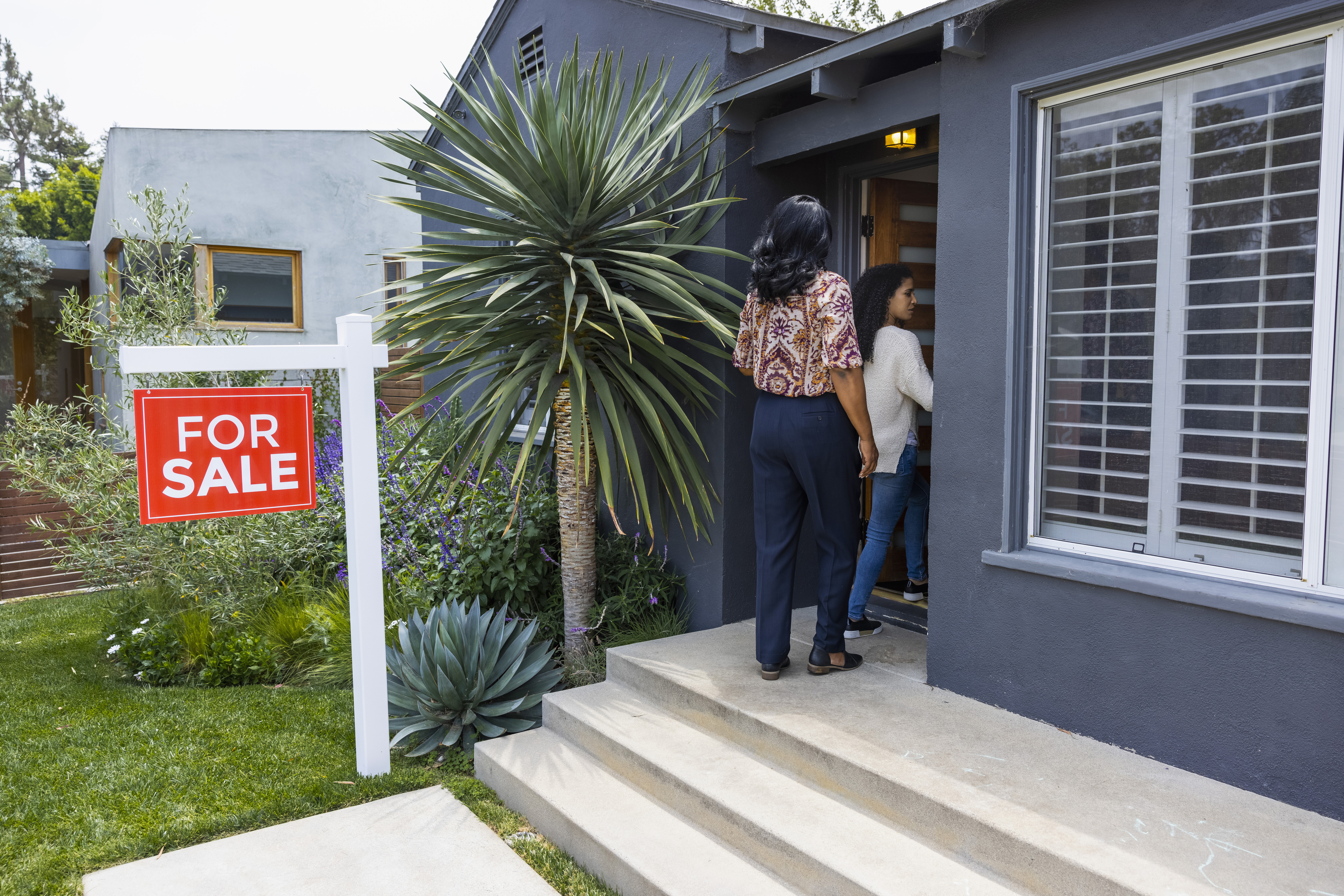 Women entering a house with a For Sale sign out front