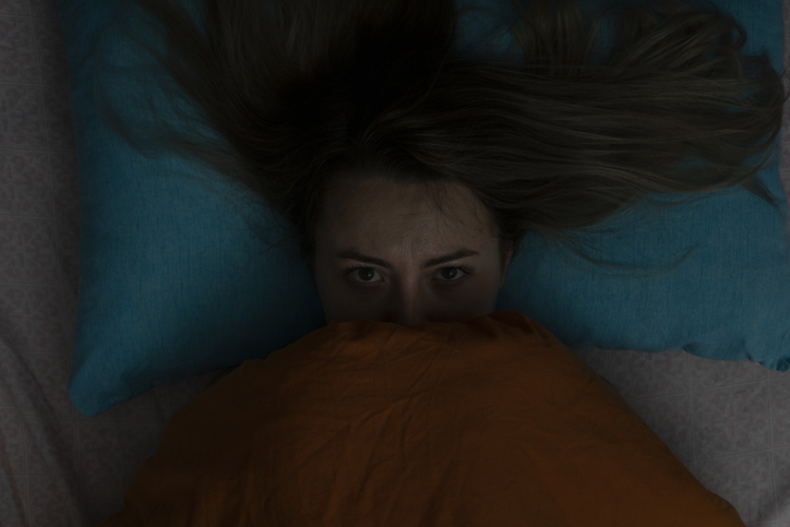 A woman in bed with the blankets pulled up to her face