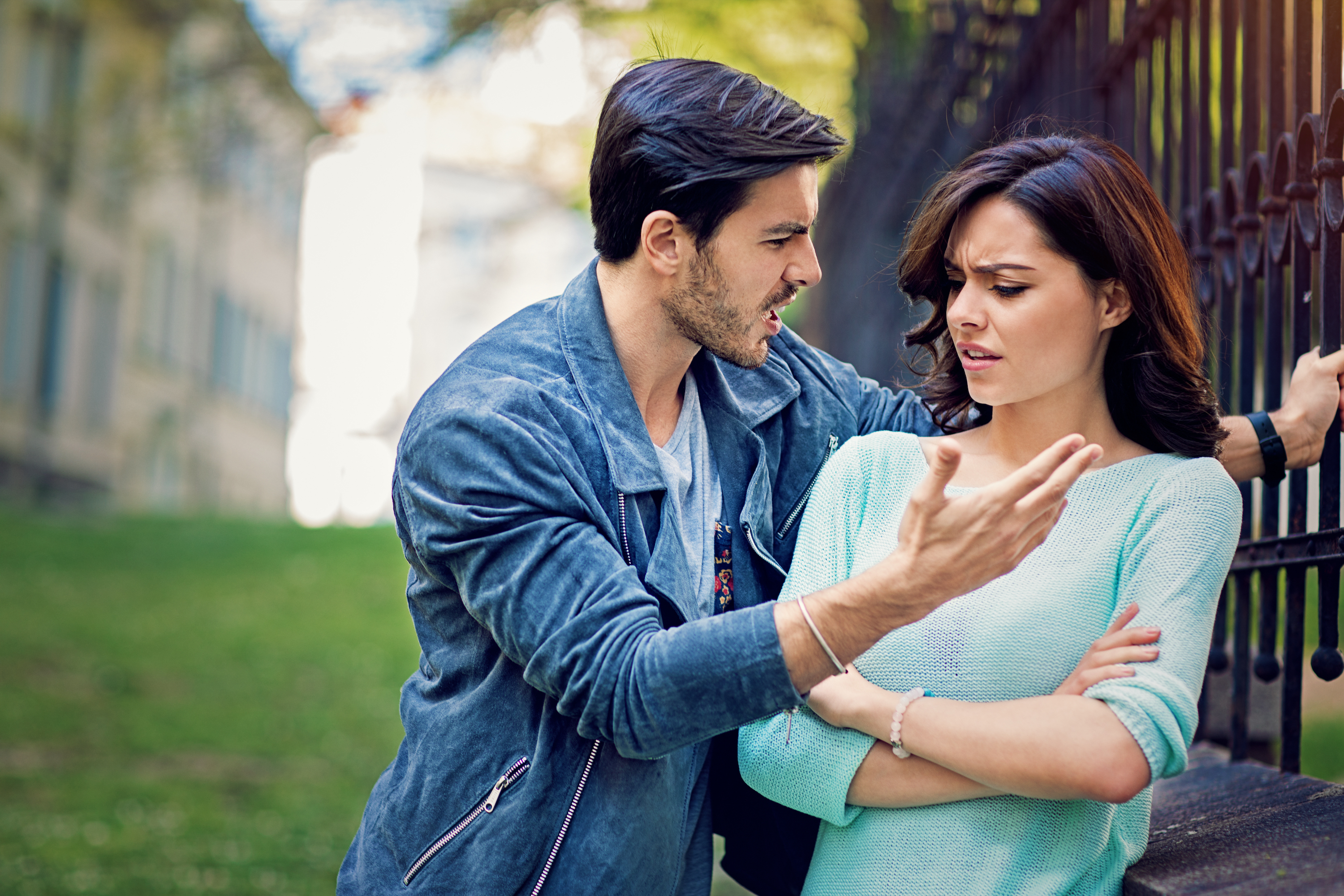 A man aggressively arguing with a woman outside near a fence