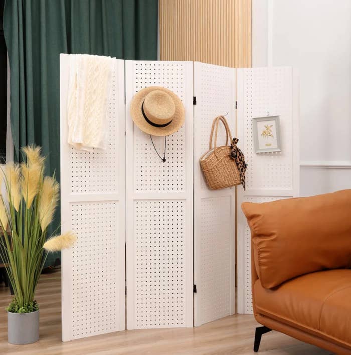 a white room divider with pegs holding a hat, purse, and picture frame