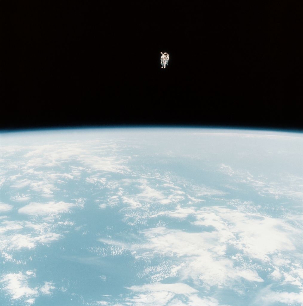 A tiny guy in a spacesuit floating above the Earth in black outerspace