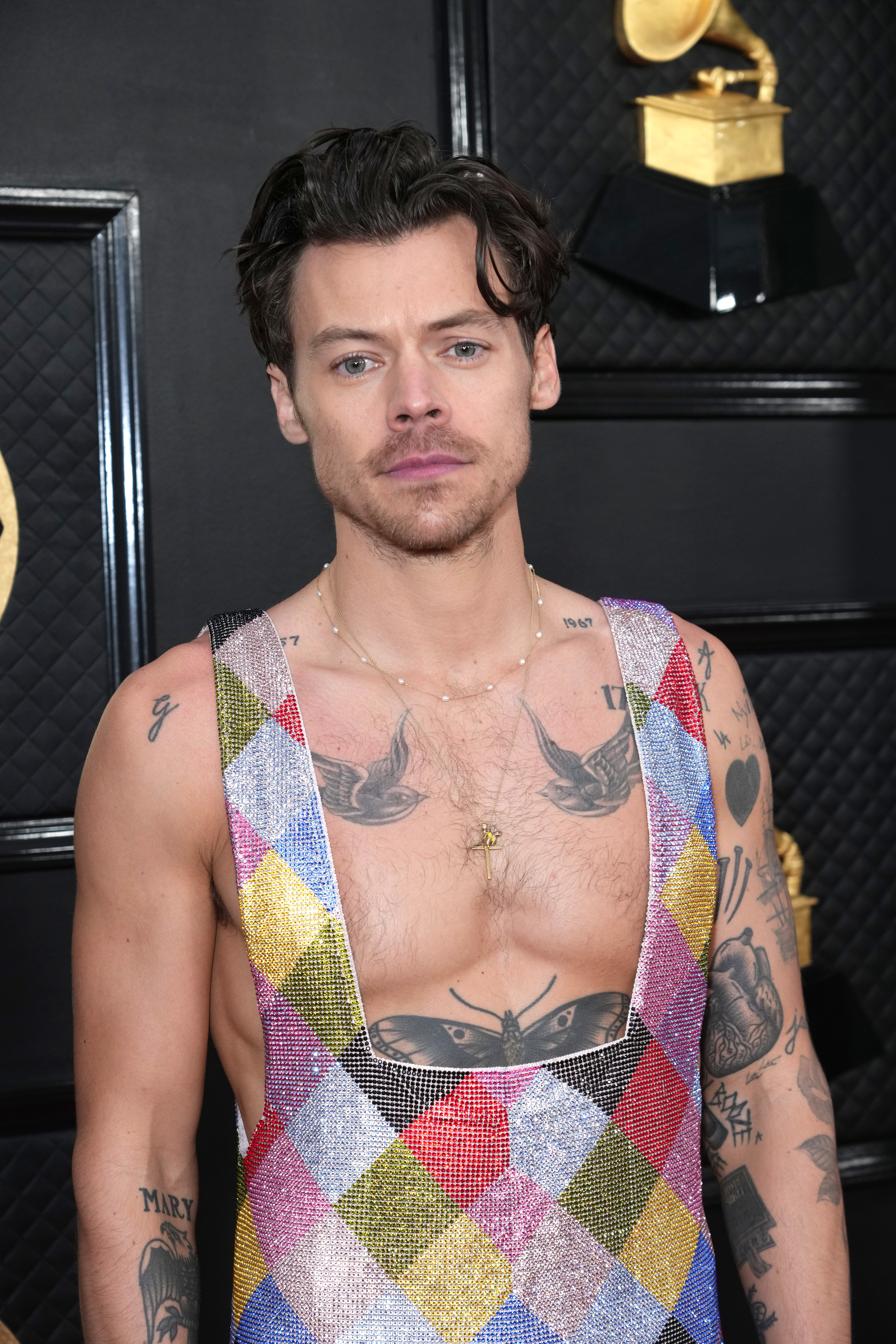 Closeup of Harry Styles at a media event in a sequined jumpsuit with a low-square cut in the front