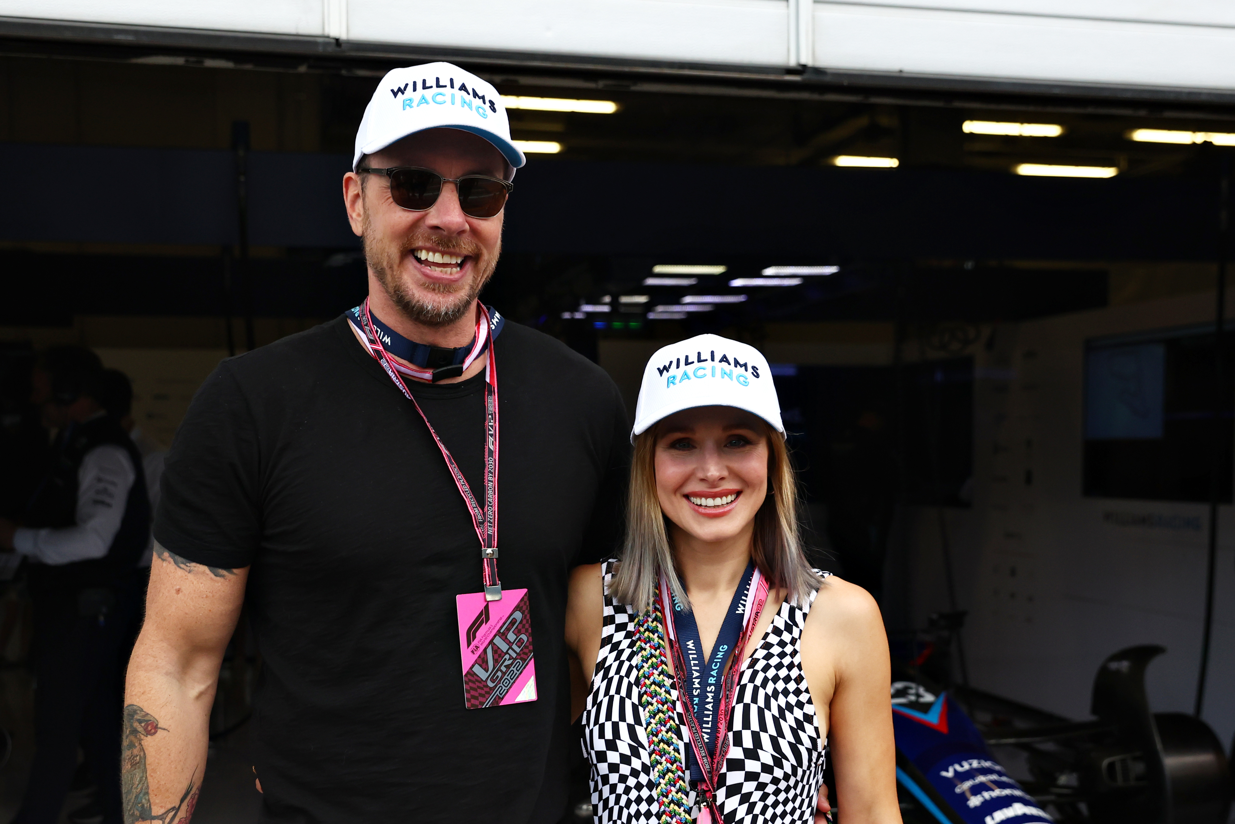 Closeup of Dax Shepard and Kristen Bell at Formula 1 race. Both are wearing. Williams Racing baseball caps