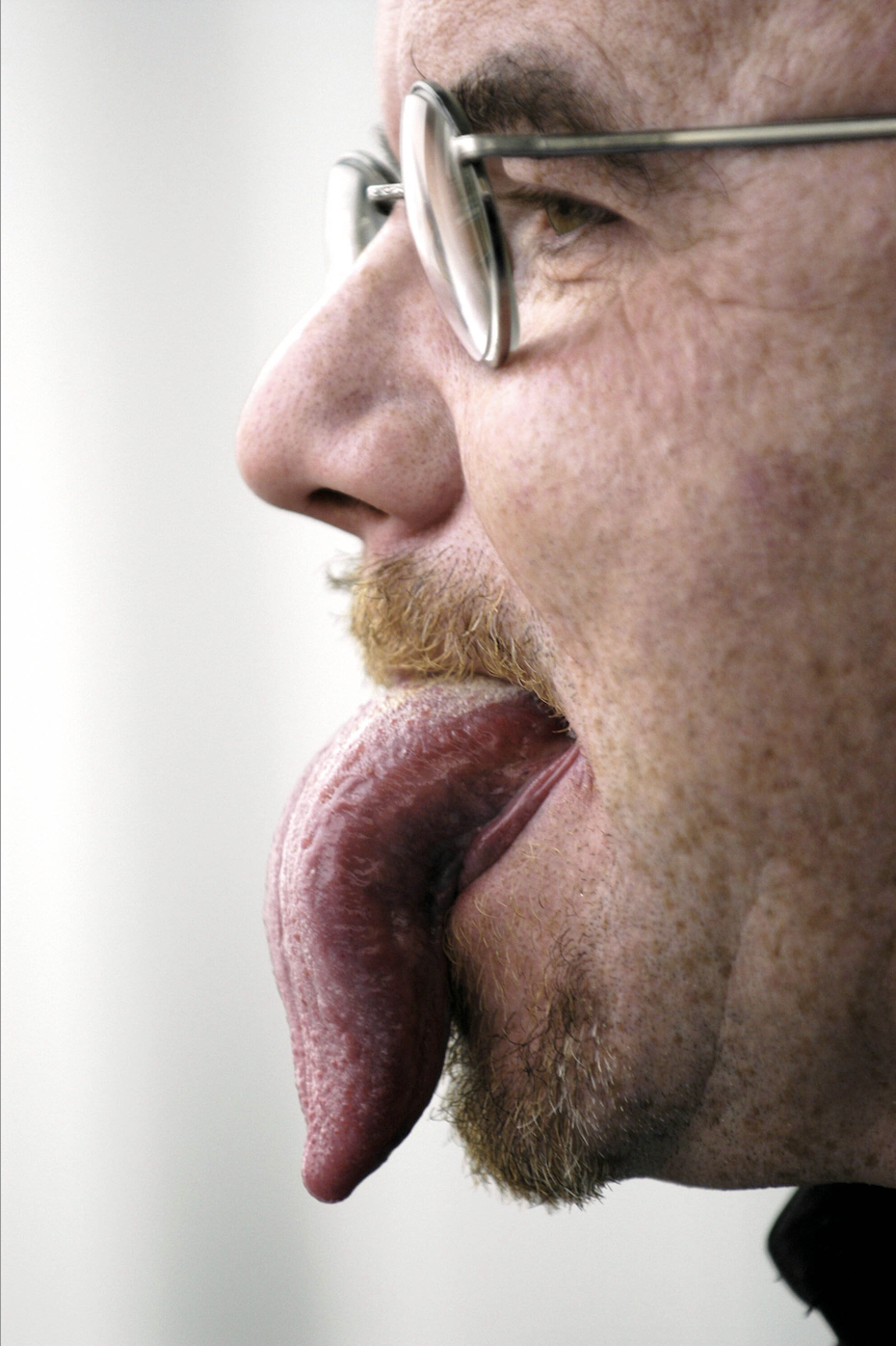 Close-up of a man&#x27;s tongue sticking out and down to the bottom of his slightly bearded chin