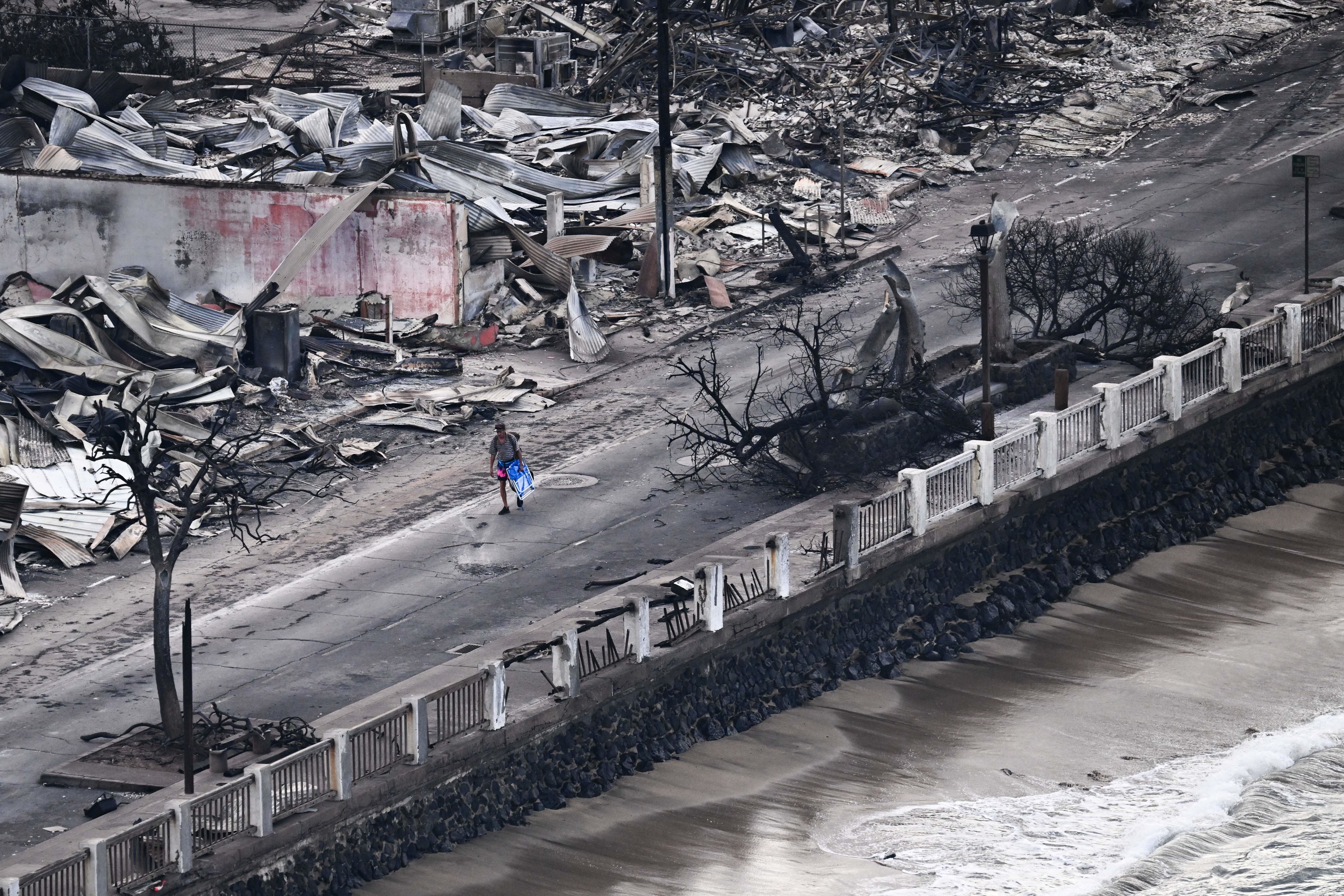 A man walking down an empty road in-between destroyed structures and the ocean