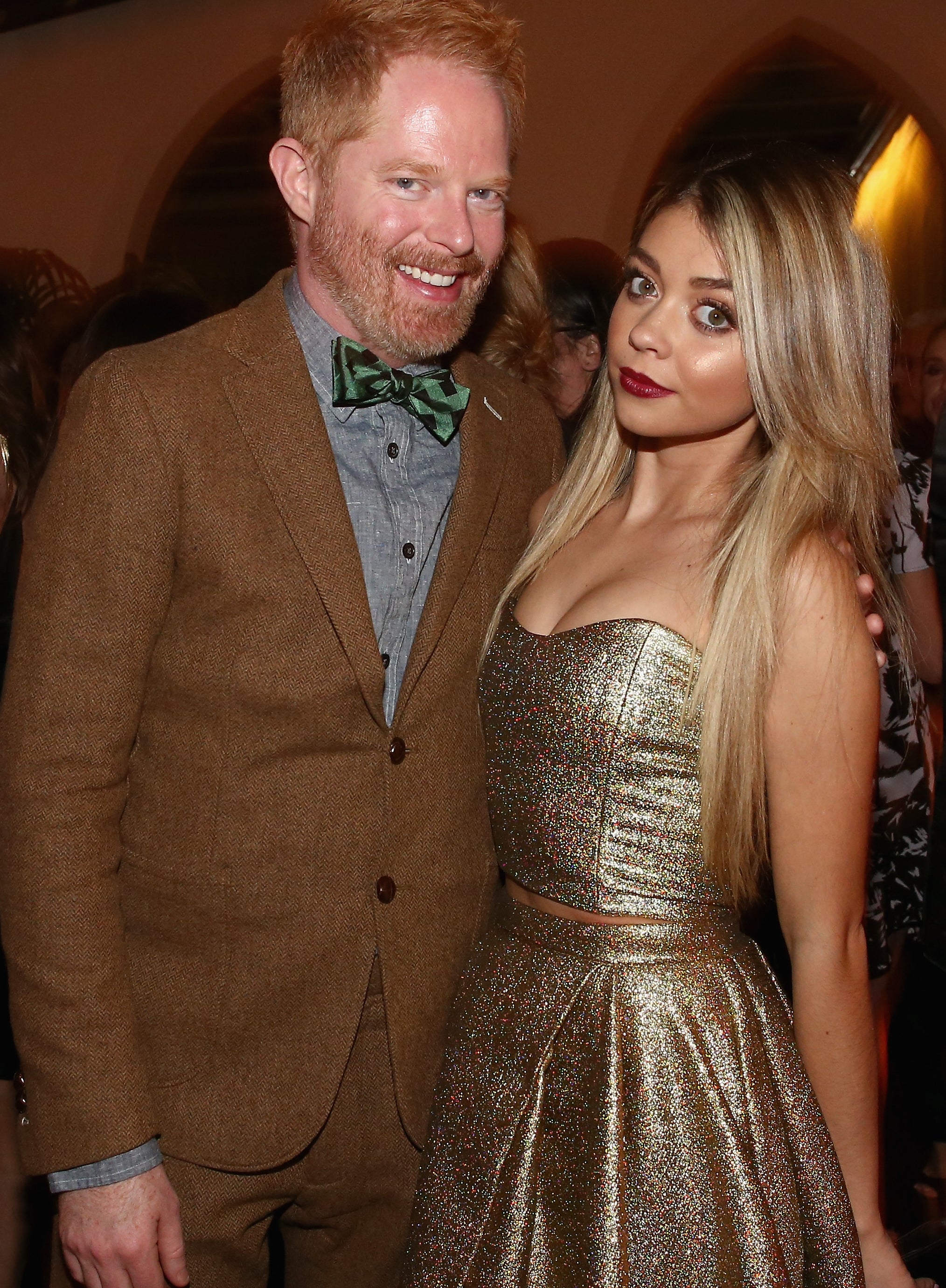 Jesse and Sarah pose for a photo together inside an event. Jesse is wearing a suit and bowtie and Sarah is wearing a strapless metallic top with matching skirt