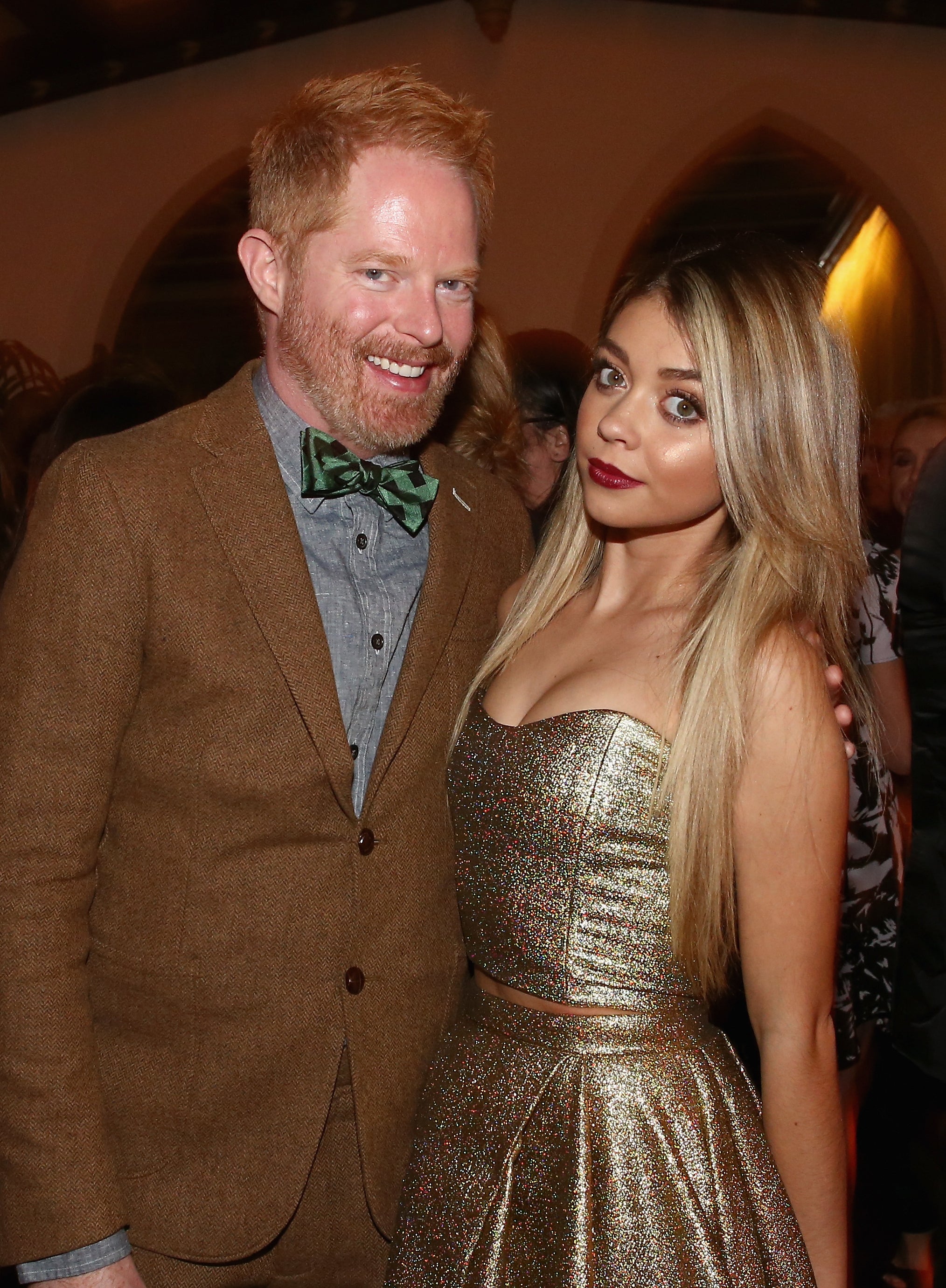 Jesse and Sarah pose for a photo together inside an event. Jesse is wearing a suit and bowtie and Sarah is wearing a strapless metallic top with matching skirt