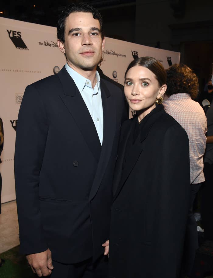 Ashley Olsen and Louis Eisner at an event. Ashley is in a long minimalist coat with her hair pulled back and Louis is wearing a casual blazer