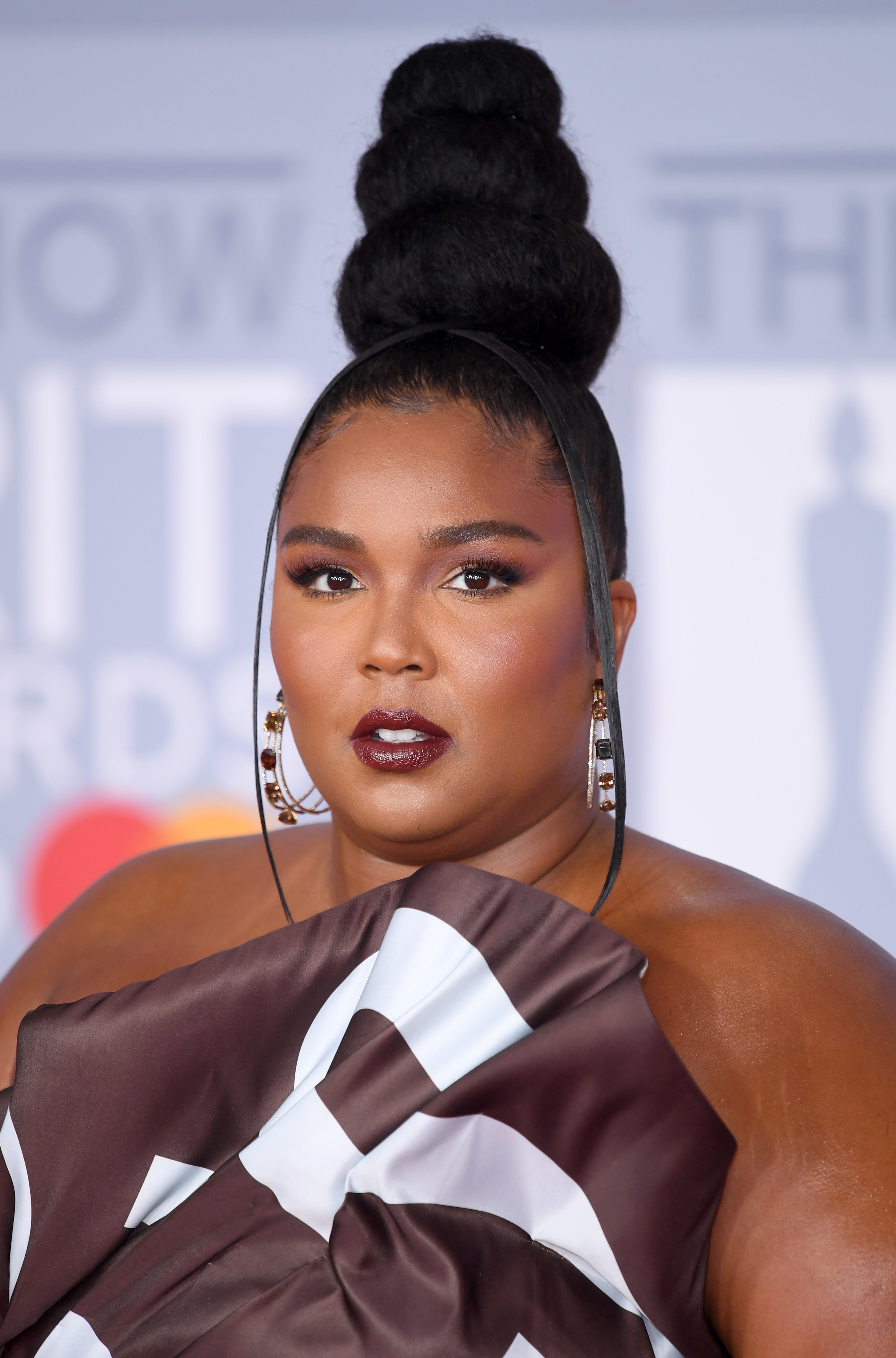 Closeup of Lizzo on the red carpet with her hair pulled into a three-tiered top knot with thing tendrils
