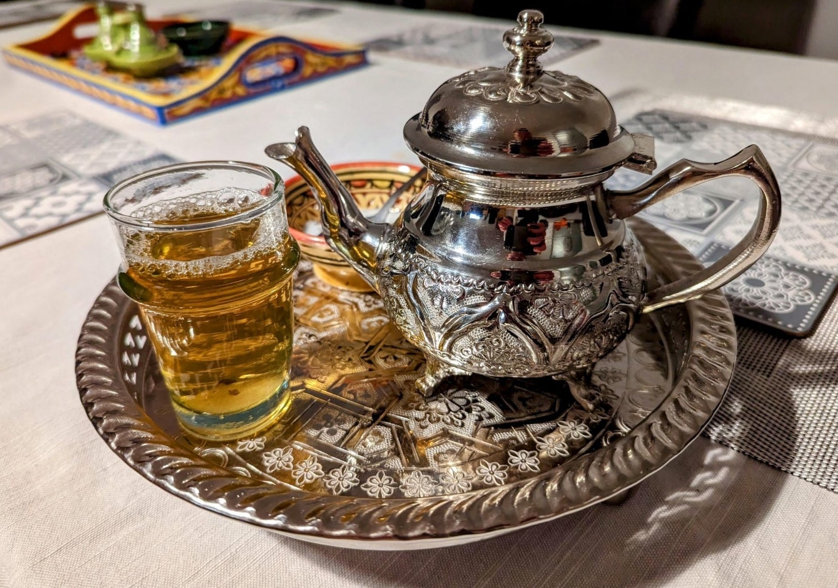 A glass of mint tea next to the kettle that brewed it