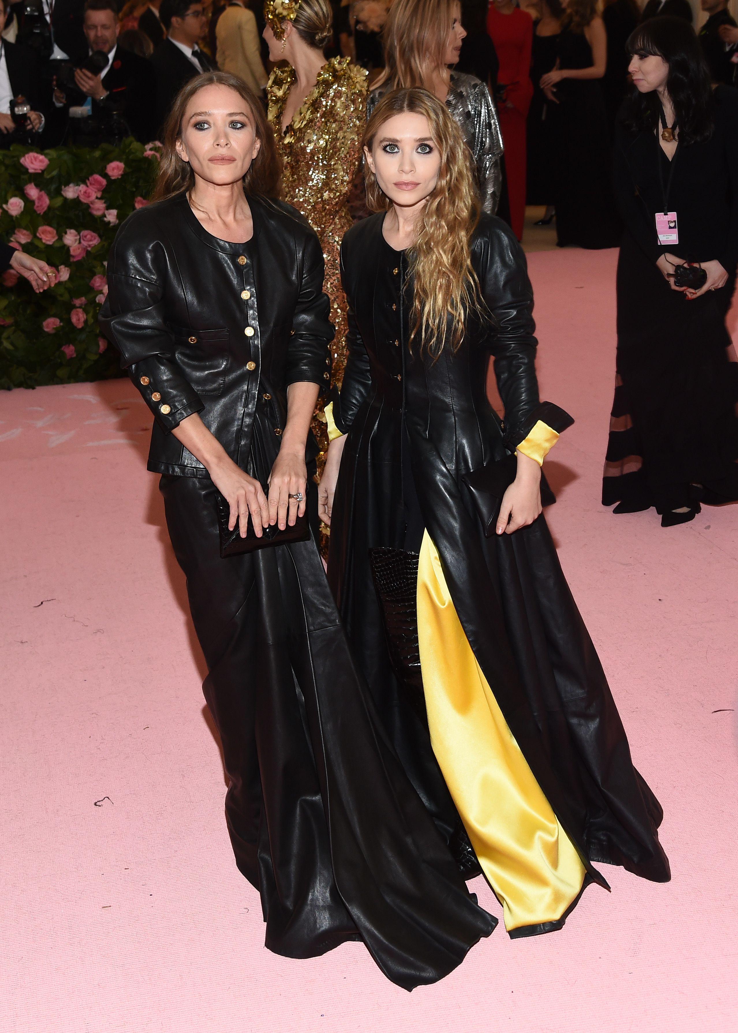 The twins stand together as photographers take their picture on the Met Gala red carpet. They're both wearing leather dresses with button detailing