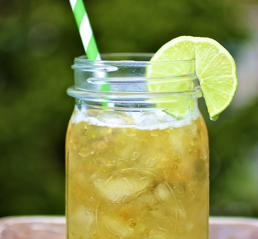 A glass of lulada sits on a table with a lime wedge on the rim and a straw