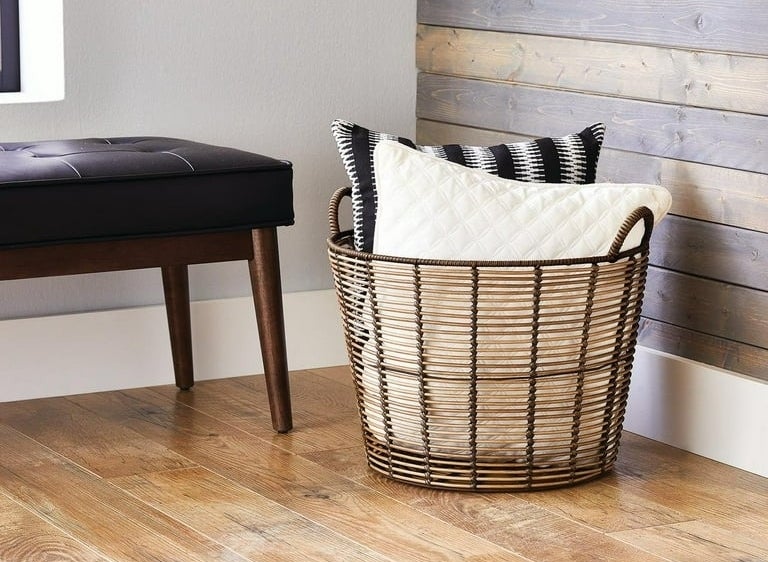 brown storage basket filled with pillows in a room corner