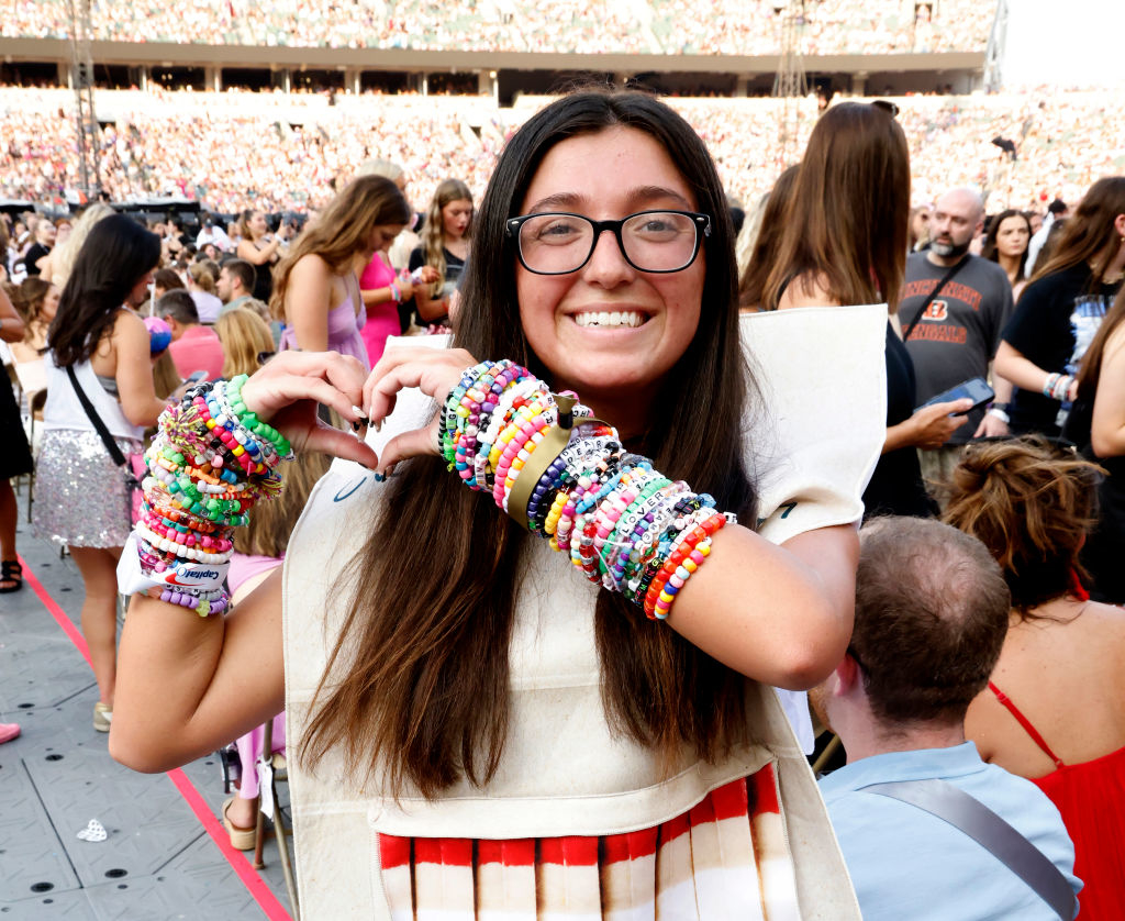 A fan wearing a ton of friendship bracelets holding up a heart