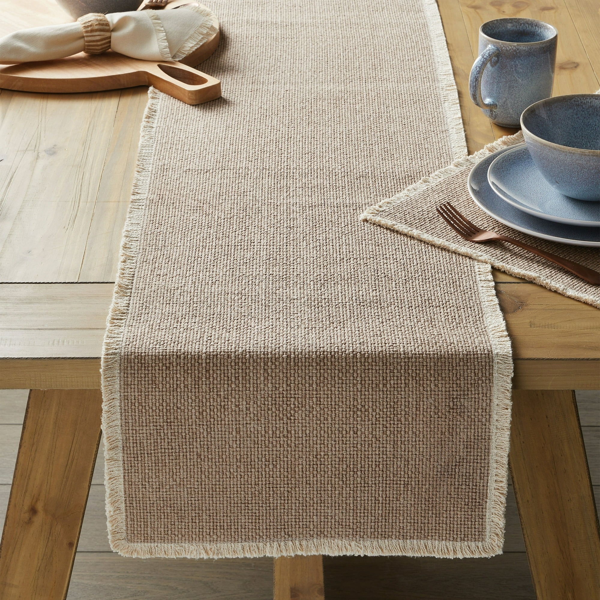 a woven table runner with fringe on a dining table