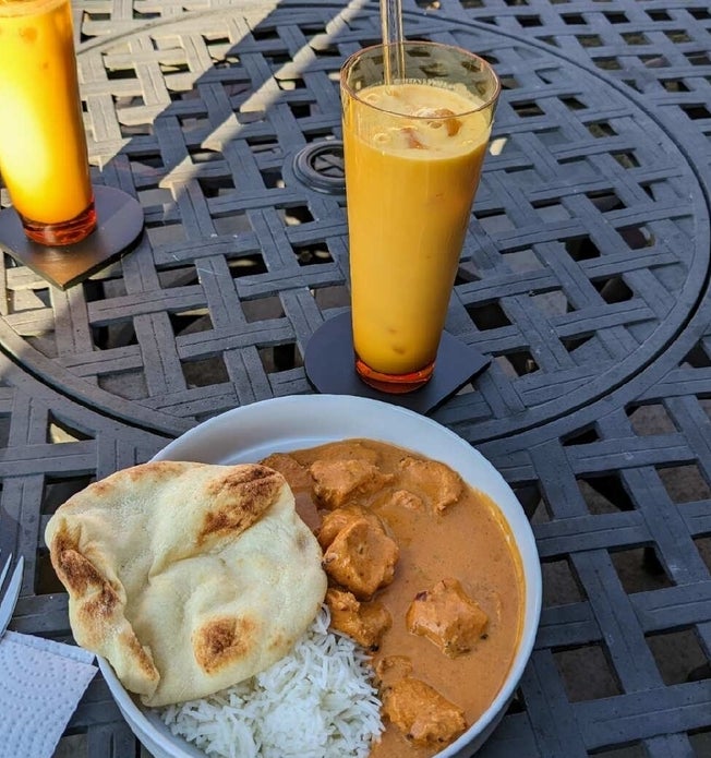 A tall glass of mango lassi is paired with a plate of butter chicken
